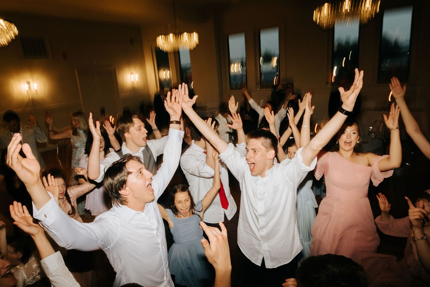 Energetic wedding guests with raised arms dancing and celebrating at a reception.