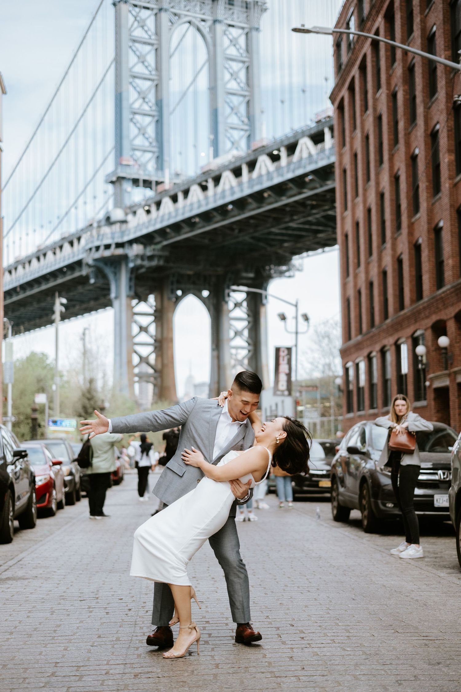 A romantic dance pose on a cobblestone street with the Manhattan Bridge creating a dramatic backdrop in DUMBO, Brooklyn.