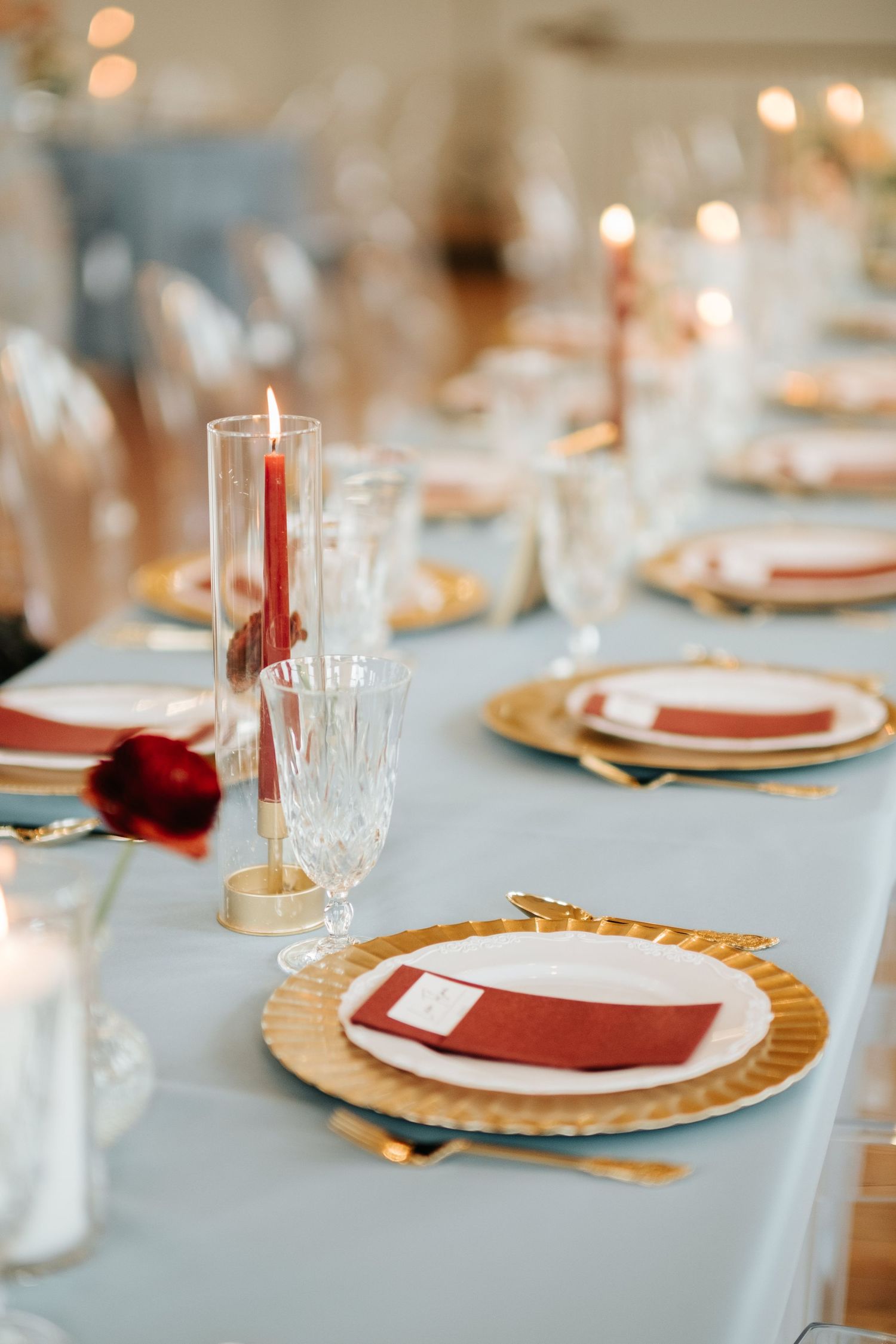 Elegant table settings with gold charger plates, white dishes, and red napkins on a light blue tablecloth.