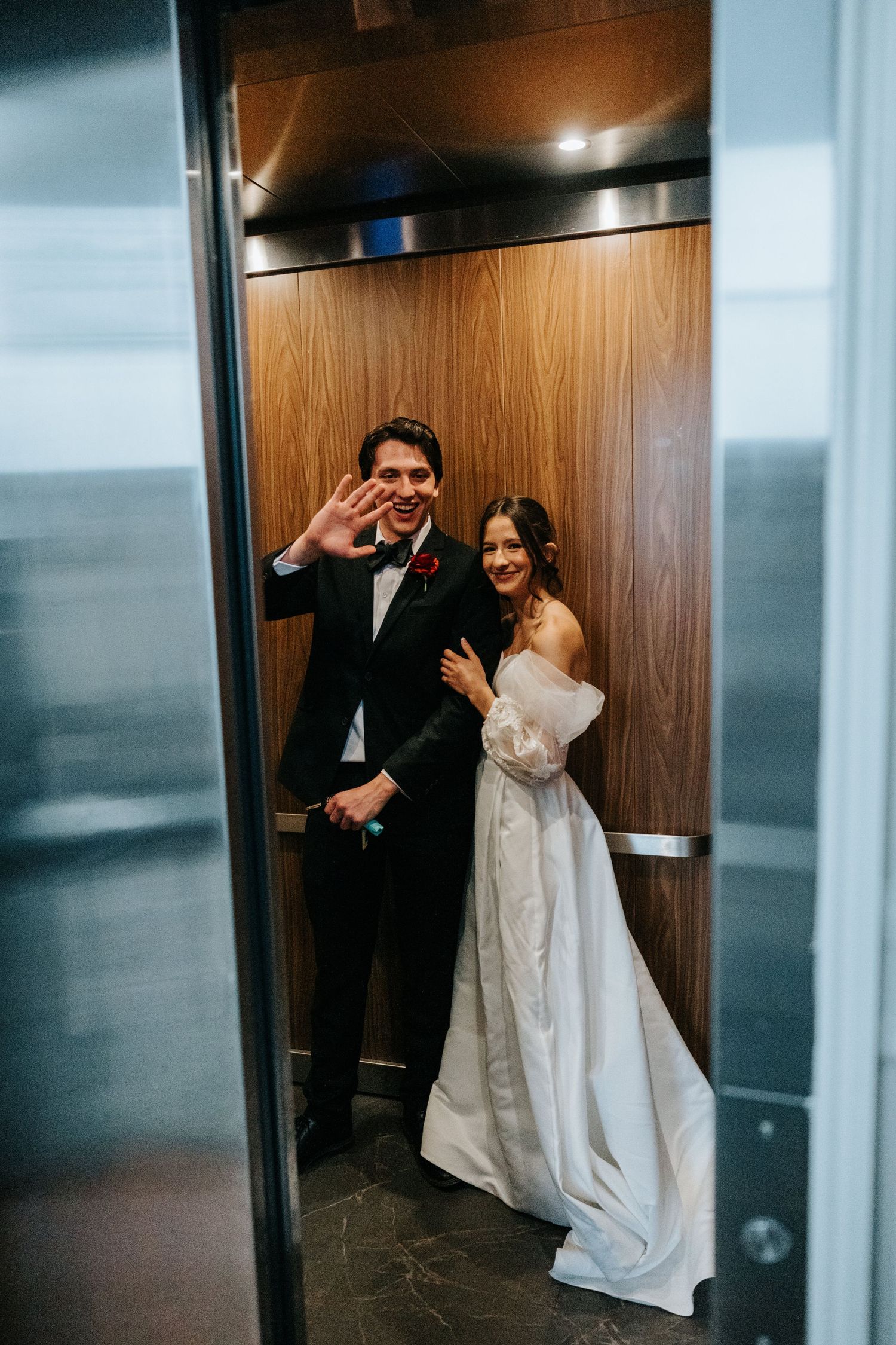 Playful couple in wedding attire shares intimate moments in an elevator during their special day.