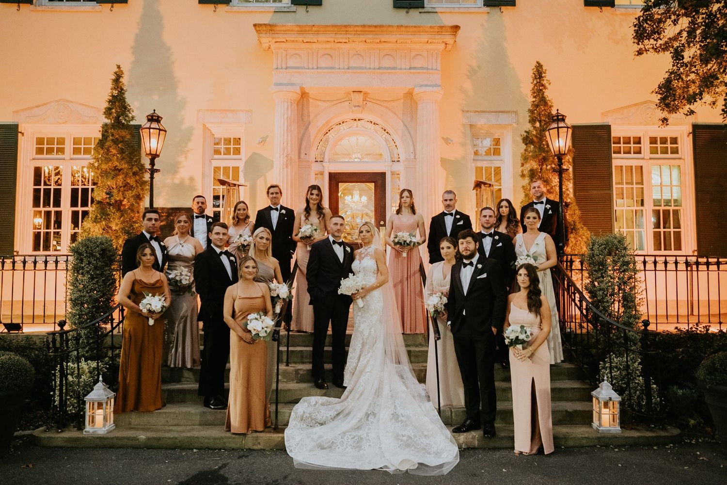Wedding party poses on illuminated venue steps at night, bride in white gown with bridesmaids in champagne dresses.