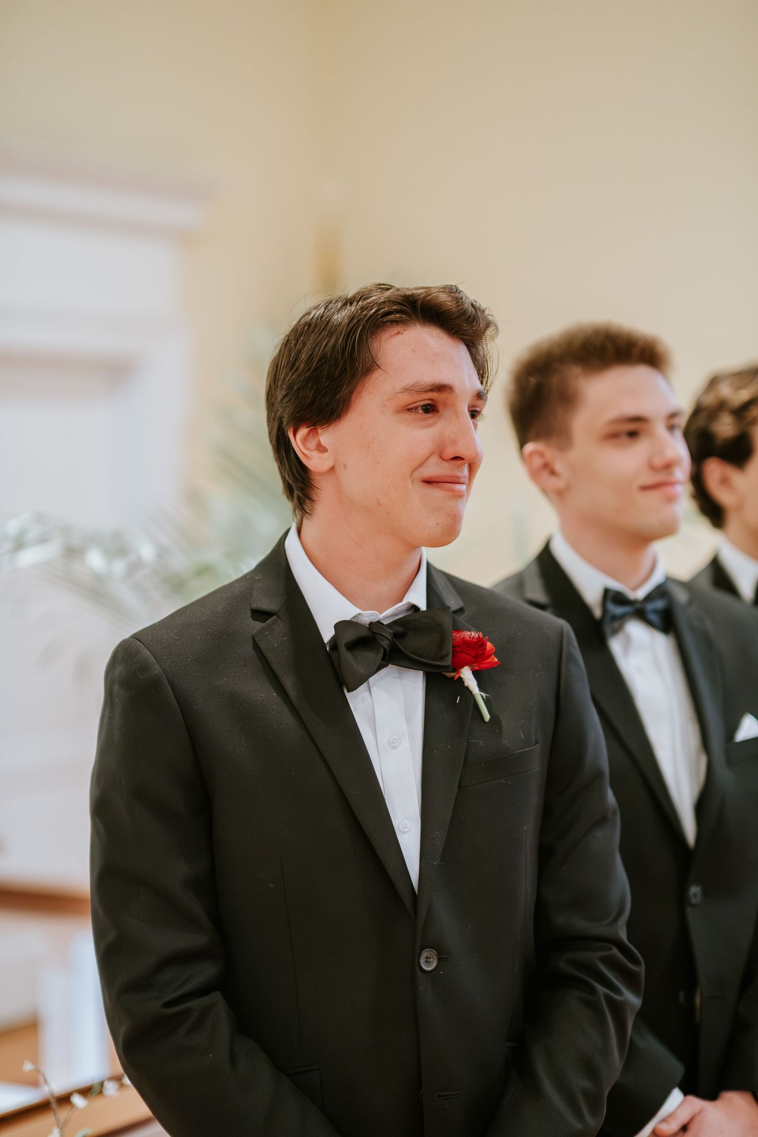Groomsmen in formal black tuxedos and bow ties at wedding ceremony.