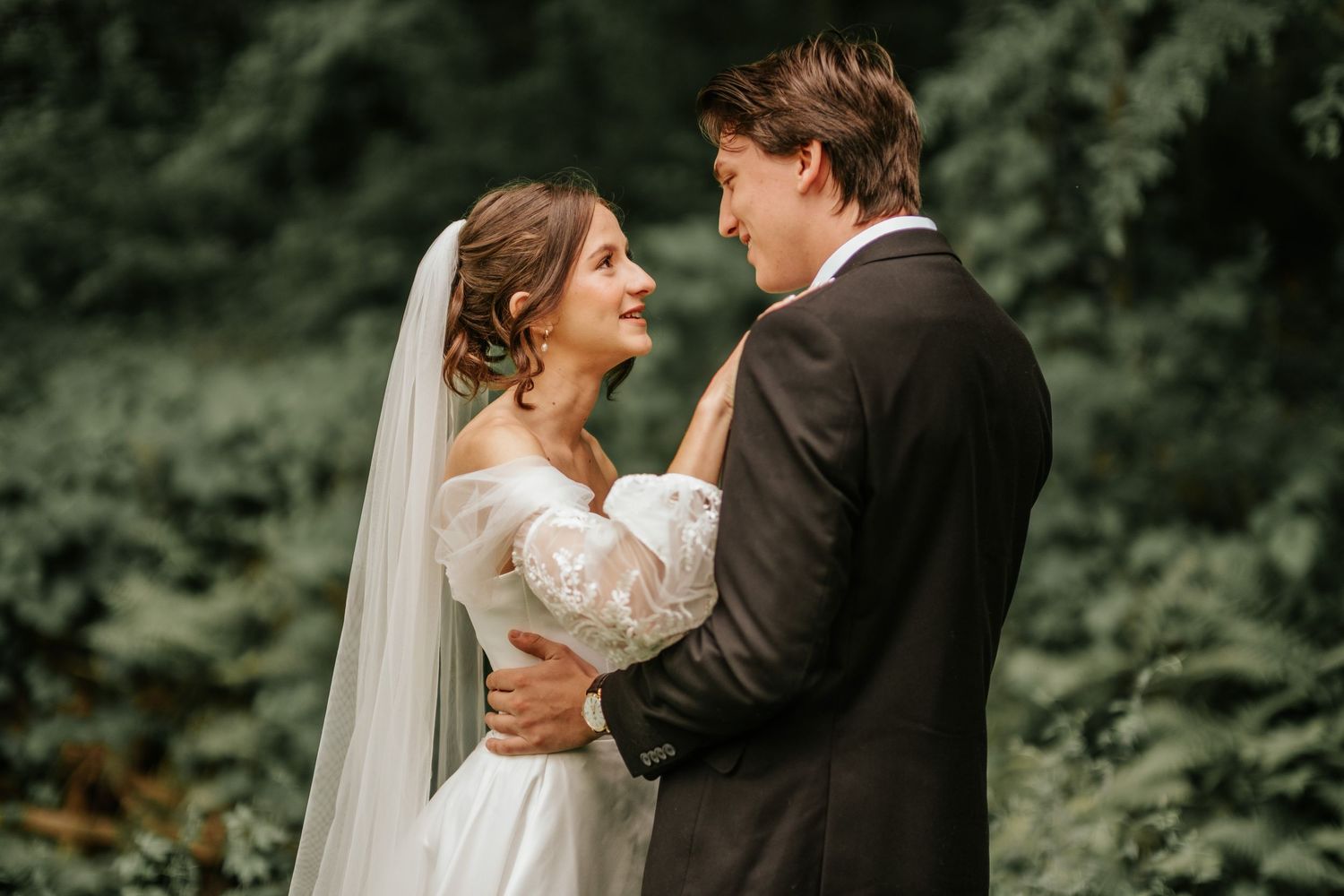 A romantic wedding moment captured in a lush green forest setting with soft natural lighting.