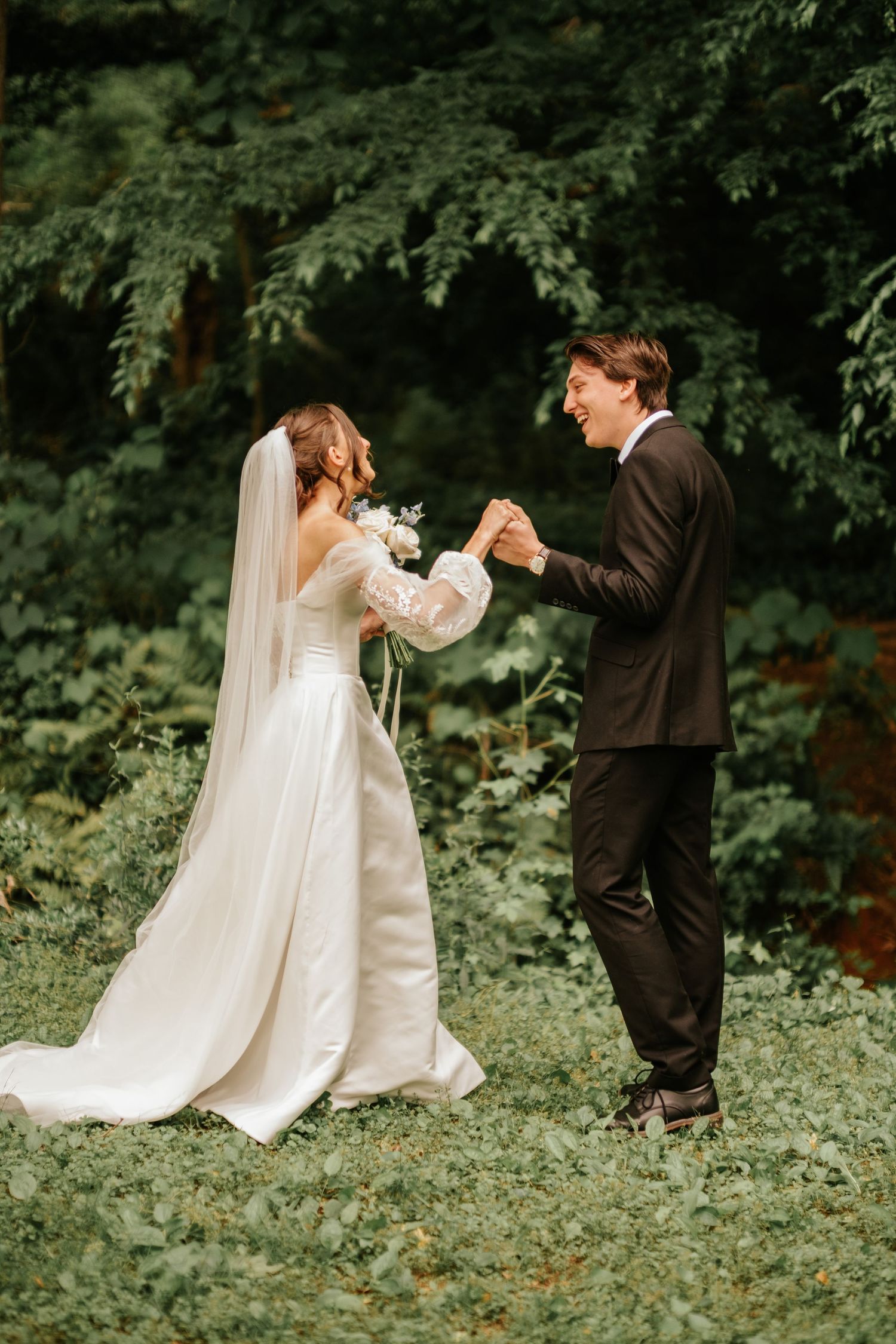 A couple in wedding attire dances together in a lush garden setting with flowing white dress and veil details.