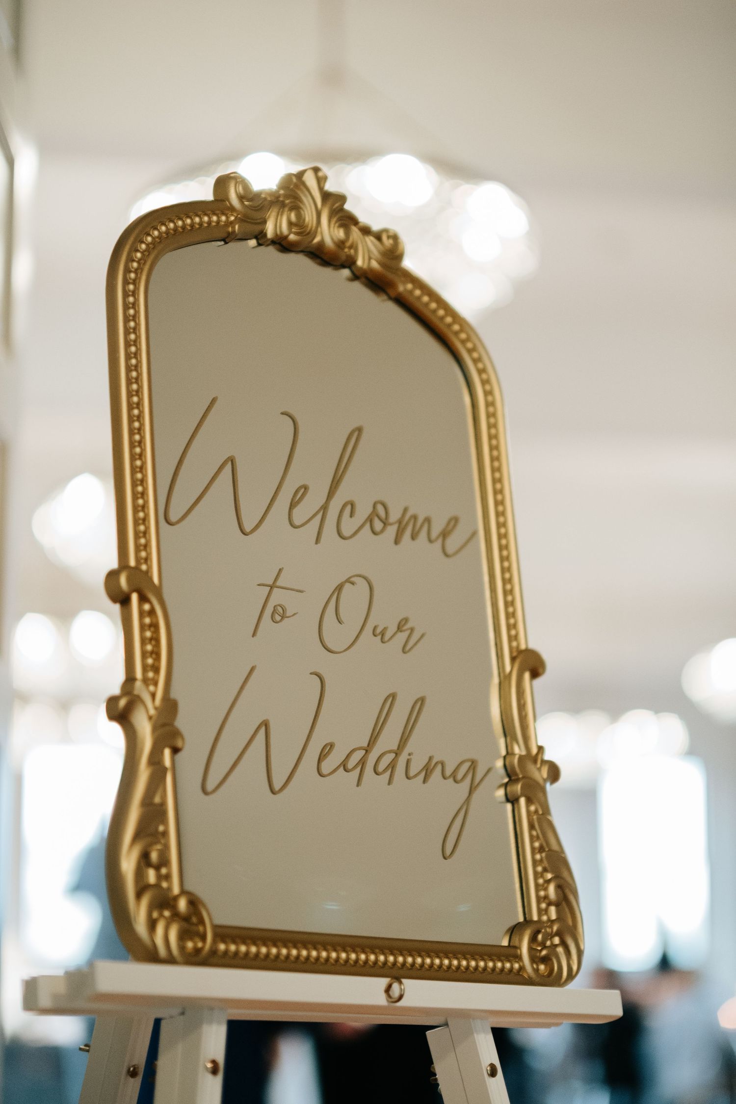 Elegant gold-framed mirror displays handwritten 'Welcome to Our Wedding' text in a romantic script style.