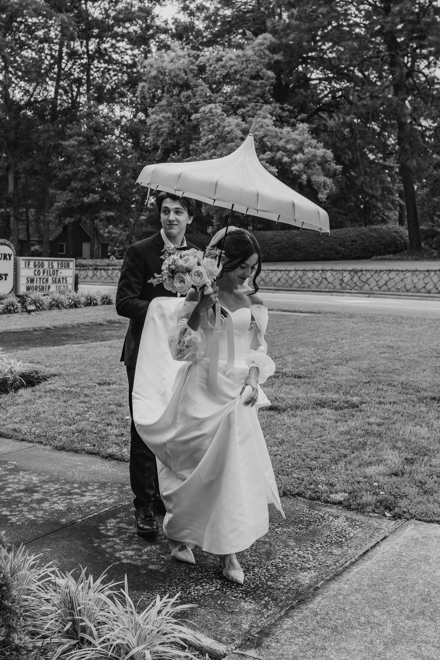 A couple shares a playful moment with umbrellas on a grassy lawn during their wedding photoshoot.