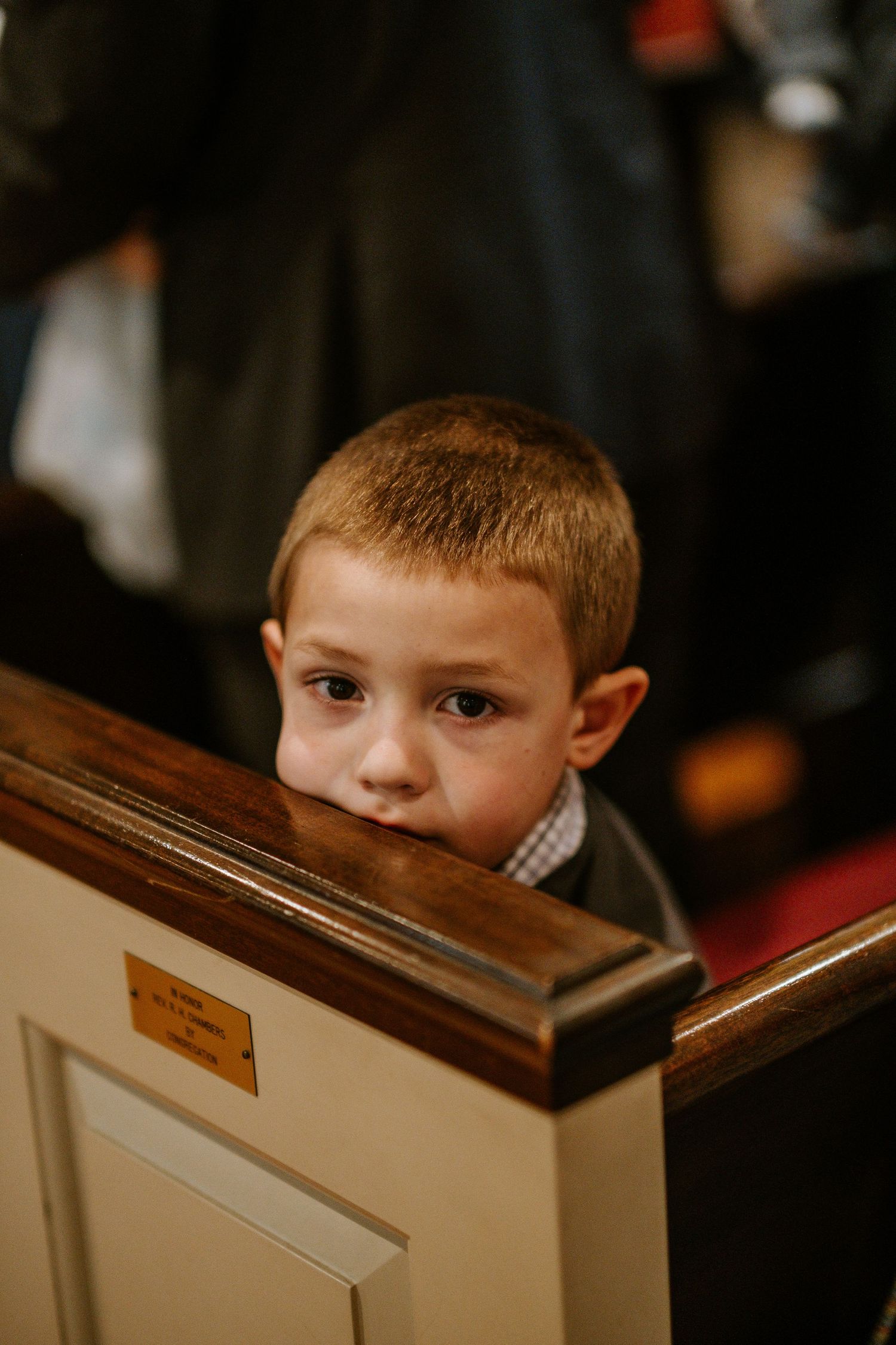A young child peeks over a wooden church pew during a service.