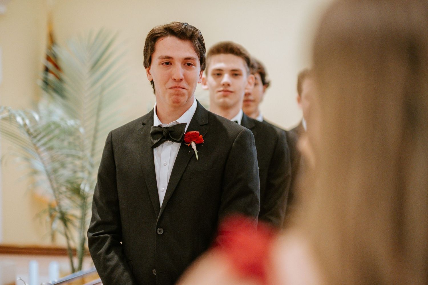 A group of formally dressed people stand in conversation during an elegant indoor event.