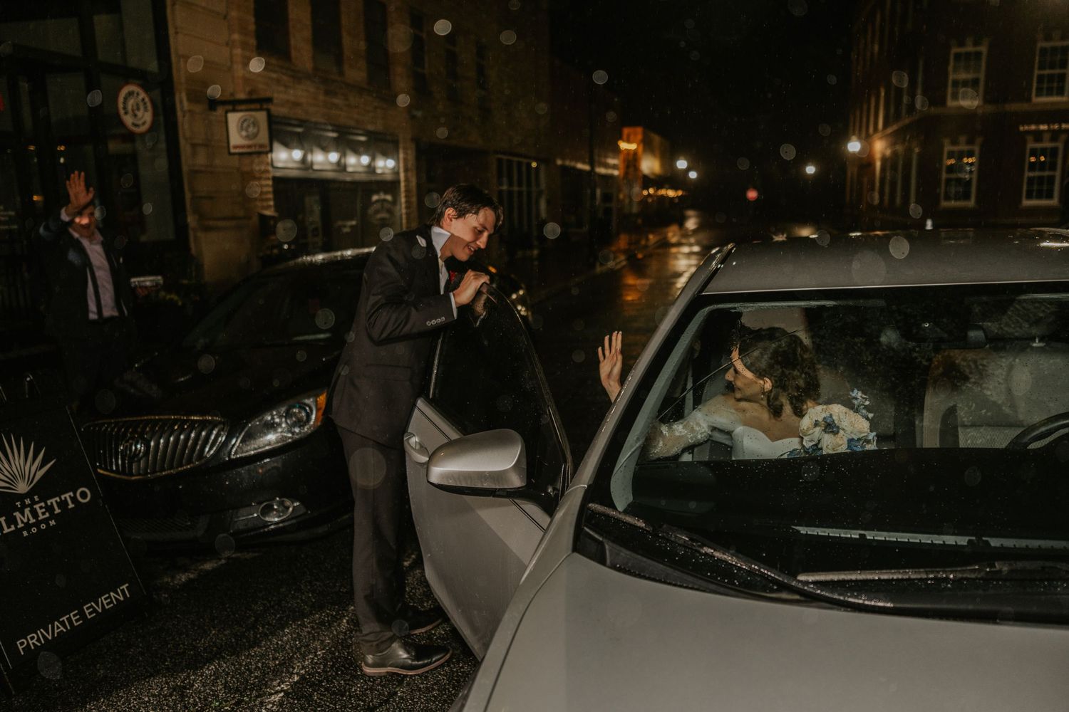 A person in a suit opens a car door at night on a city street with a dog visible inside the vehicle.