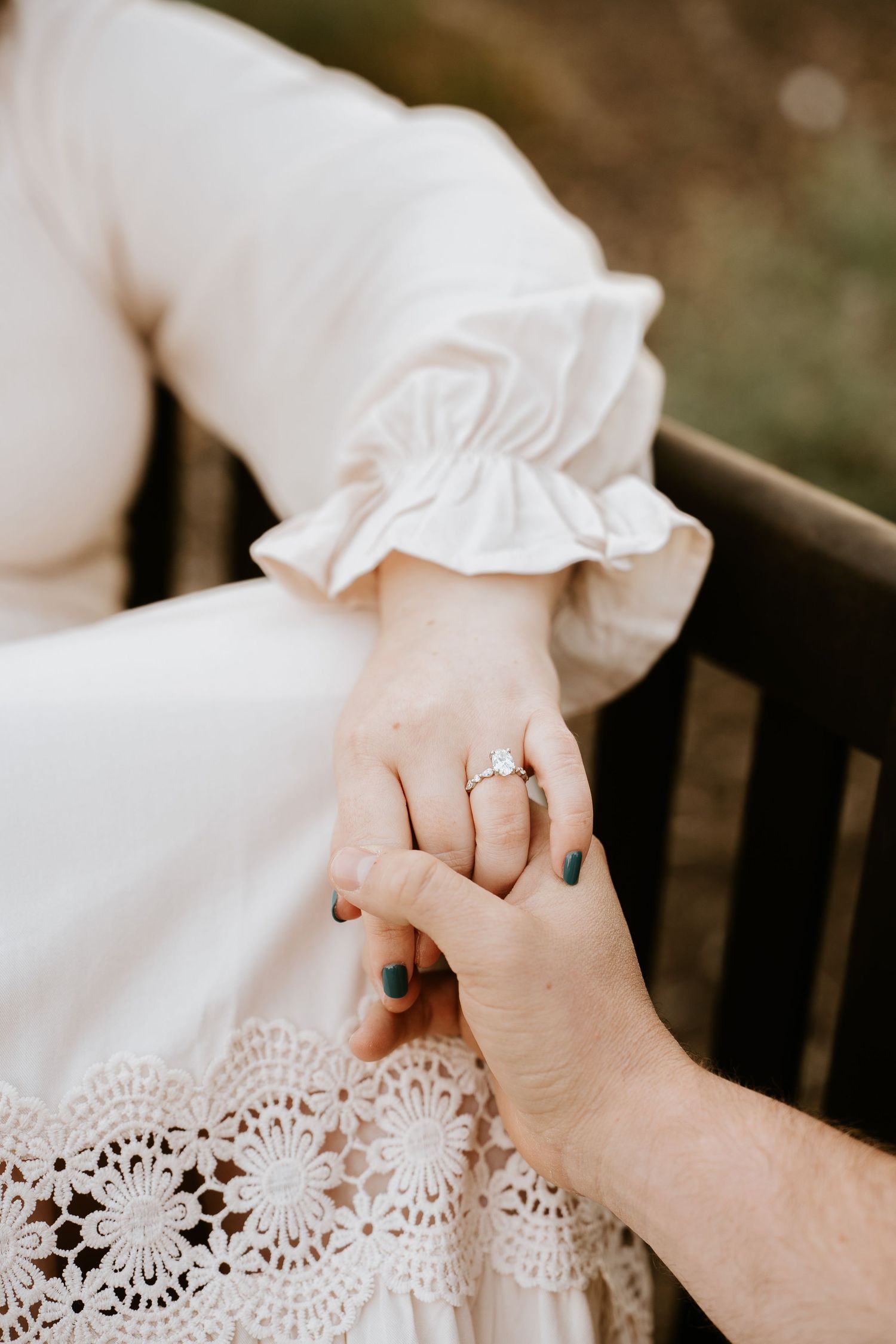 Close-up of hands with engagement ring against white lace dress fabric showing delicate details and romantic styling.