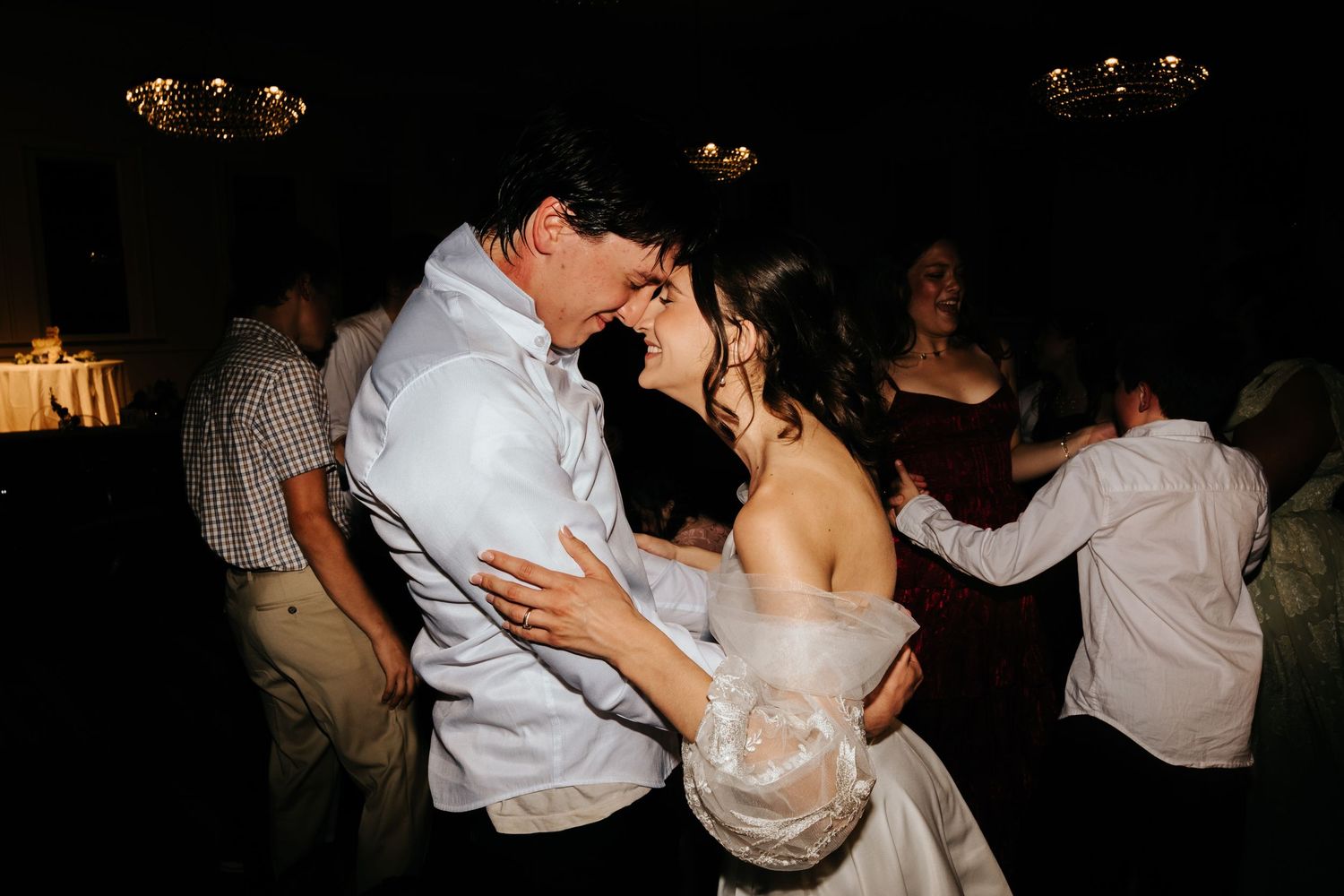 Wedding guests dancing and celebrating at a dimly lit reception venue.