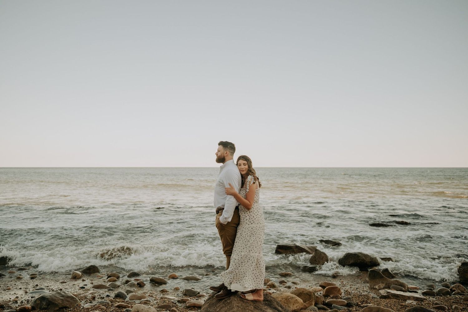 A couple embraces on a scenic coastal cliff overlooking the ocean during golden hour.