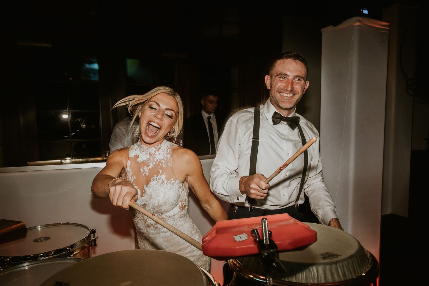 Bride and groom laughing while playing drums together at their wedding reception party.