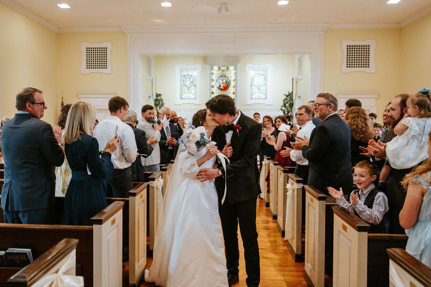 Wide angle view of a church interior with guests seated in white wooden pews.