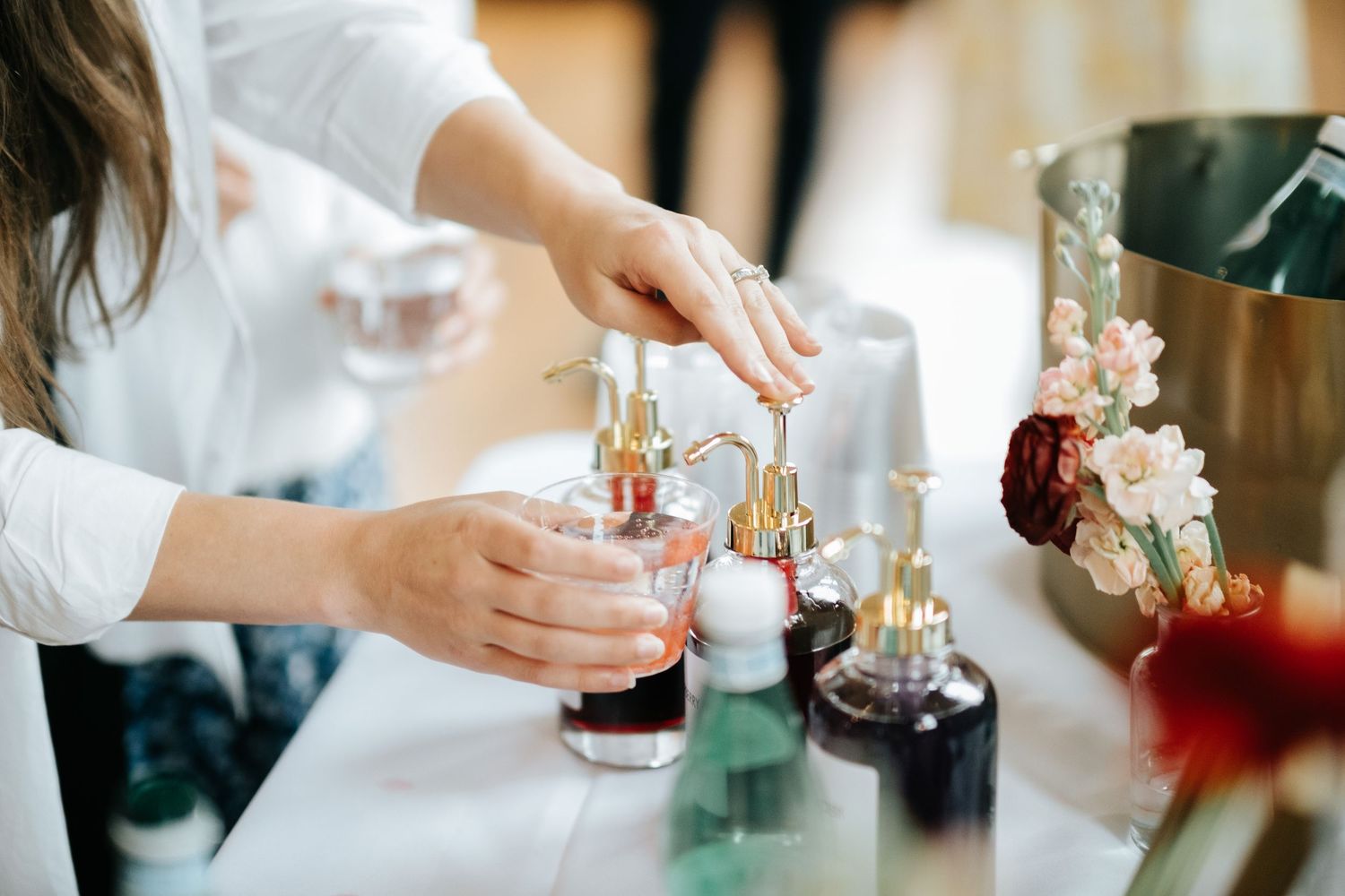 Hands pouring drinks and arranging elegant glassware at an upscale event with soft lighting and floral decor.