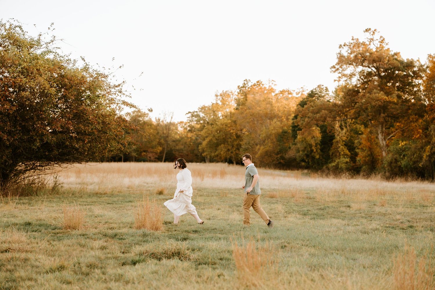 A couple runs playfully through a golden field at sunset creating a dreamy romantic atmosphere.