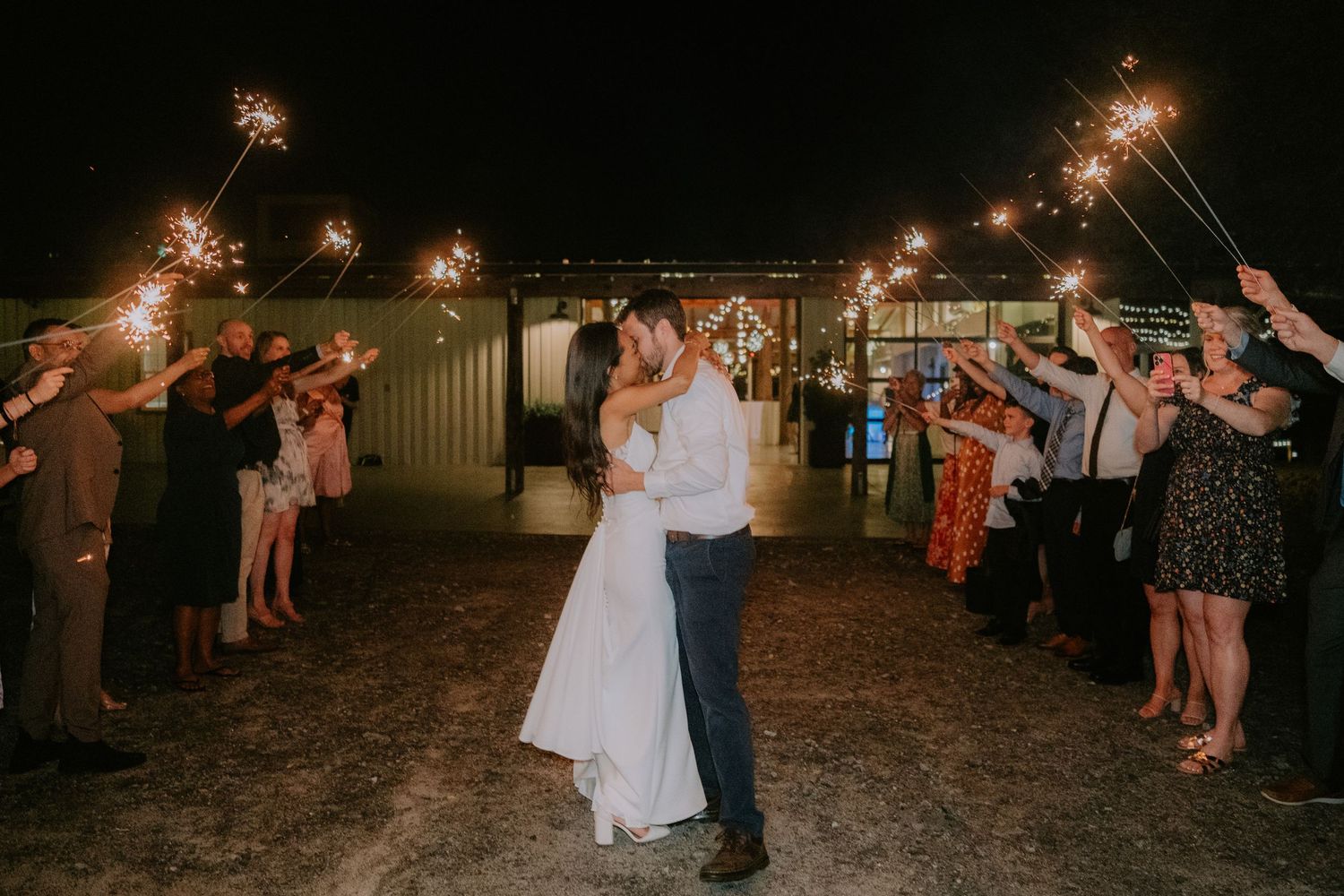 Wedding guests hold sparklers creating a magical nighttime tunnel for the newlyweds on their special evening.