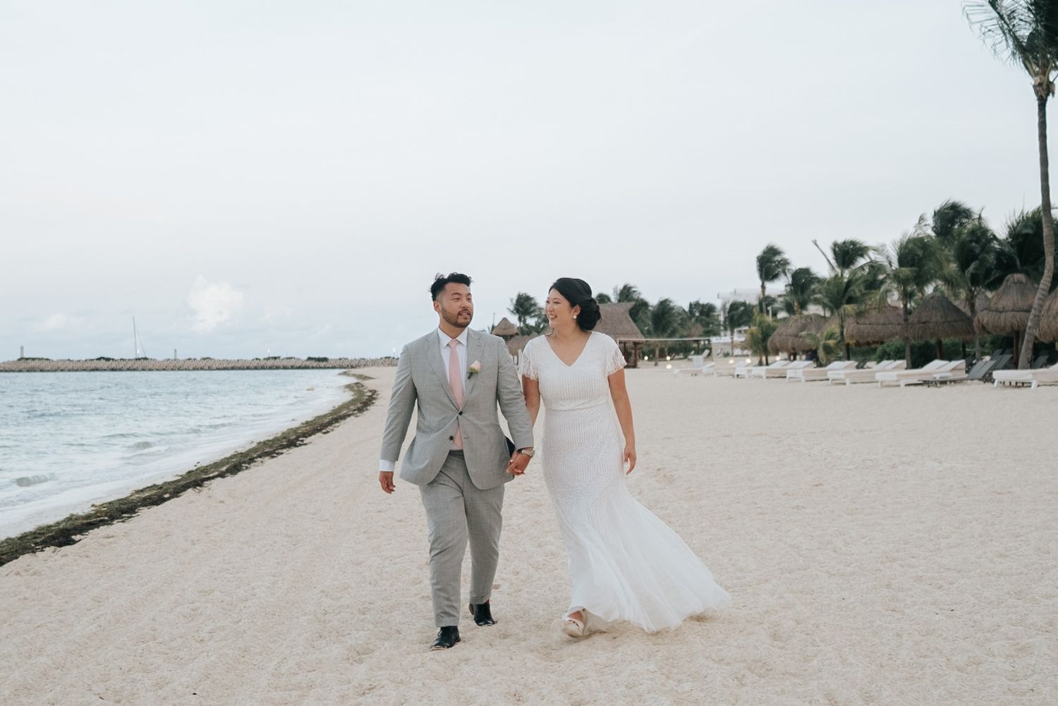 Bride and groom walk hand in hand on a sandy beach at a tropical destination wedding.
