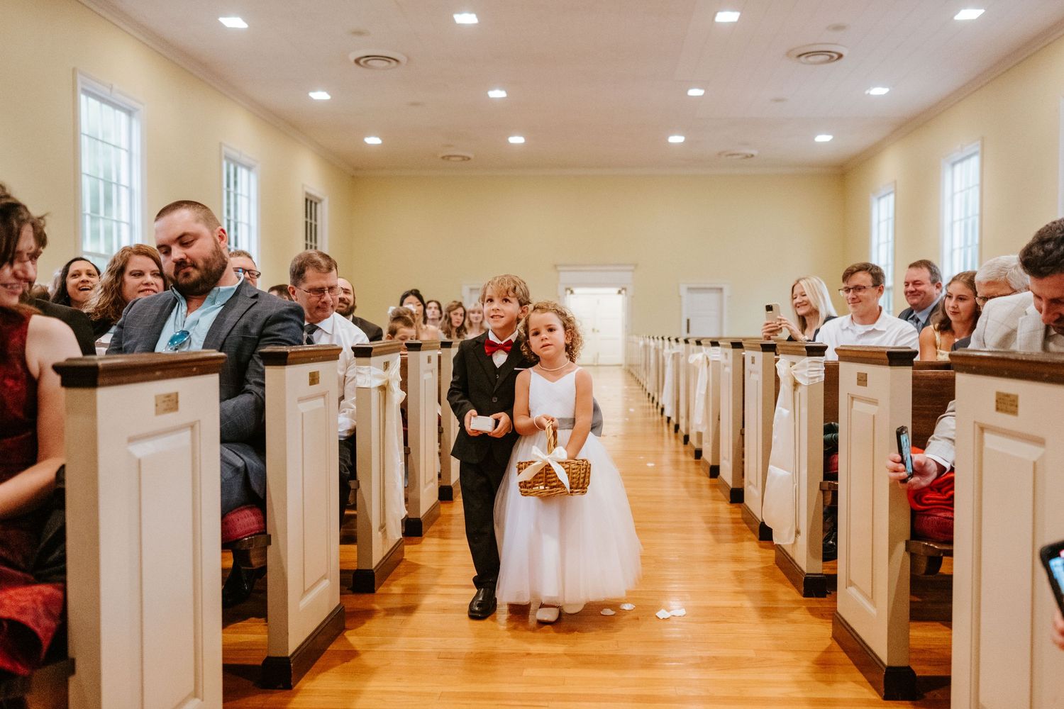 Panoramic shot of a bright church sanctuary with rows of white pews and people gathered for a ceremony.