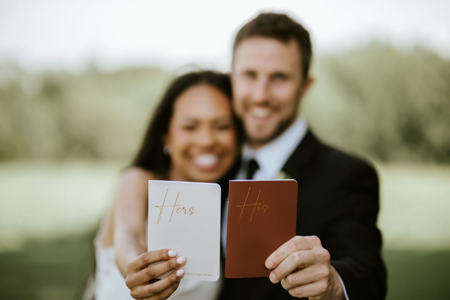 A couple holds up passport documents while standing outdoors in a natural setting.