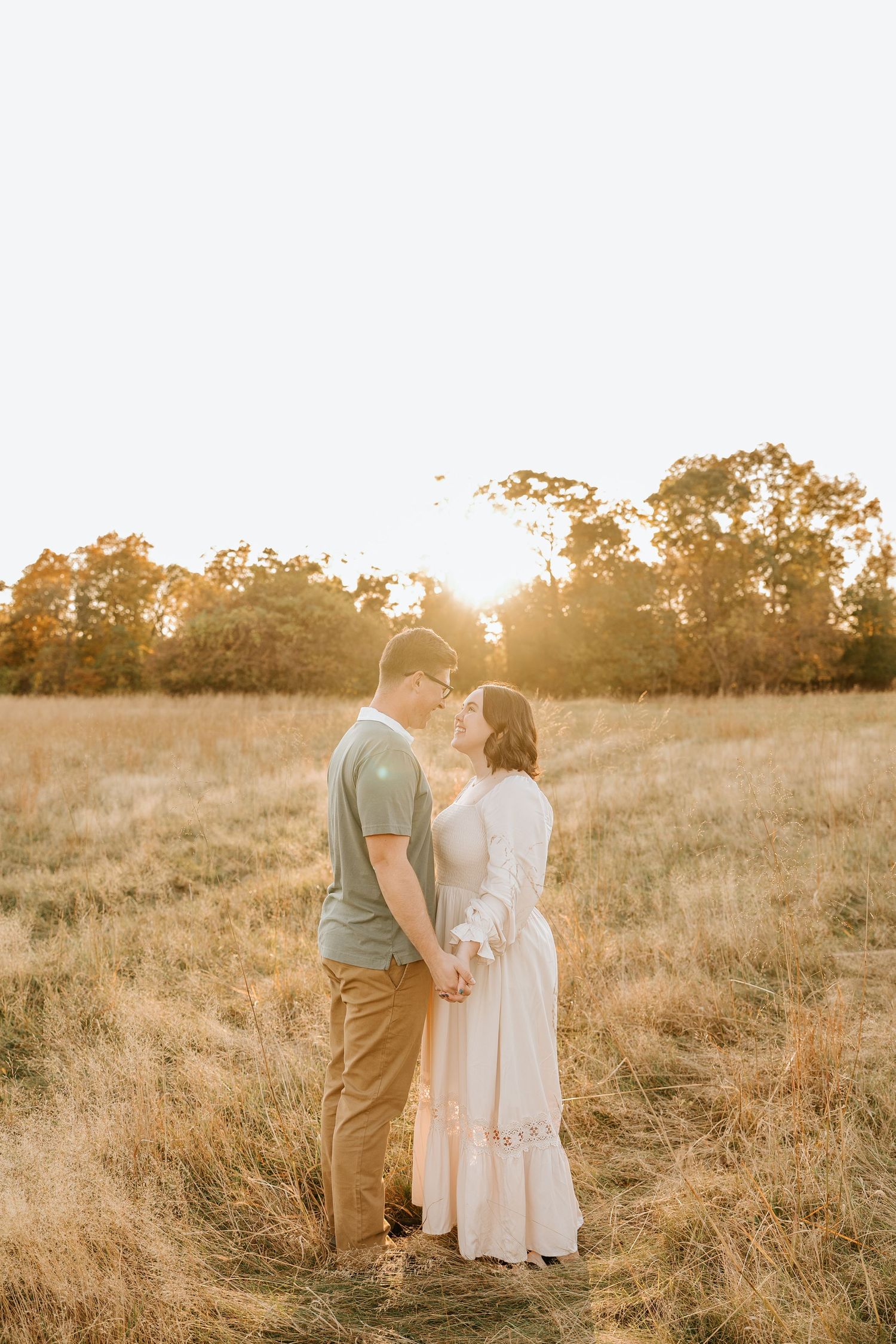 A couple embraces in a golden sunlit meadow during sunset, creating a romantic silhouette against the warm landscape.