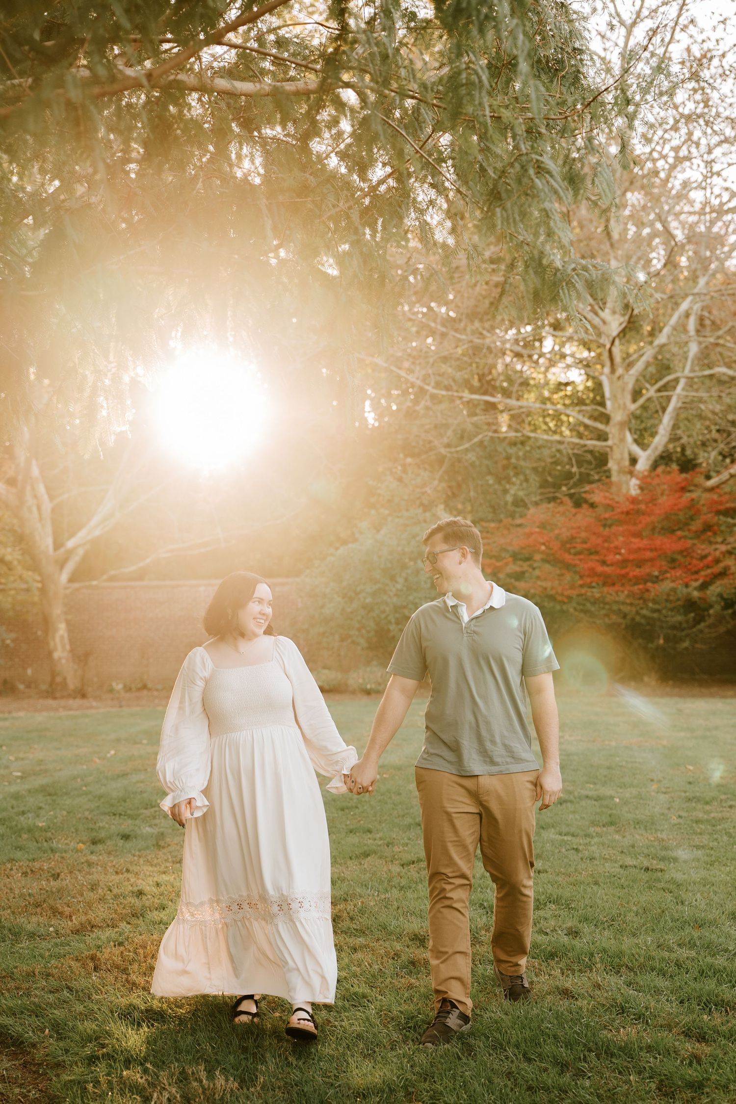 A couple walks hand in hand through a sunlit garden with autumn foliage creating a dreamy atmosphere.