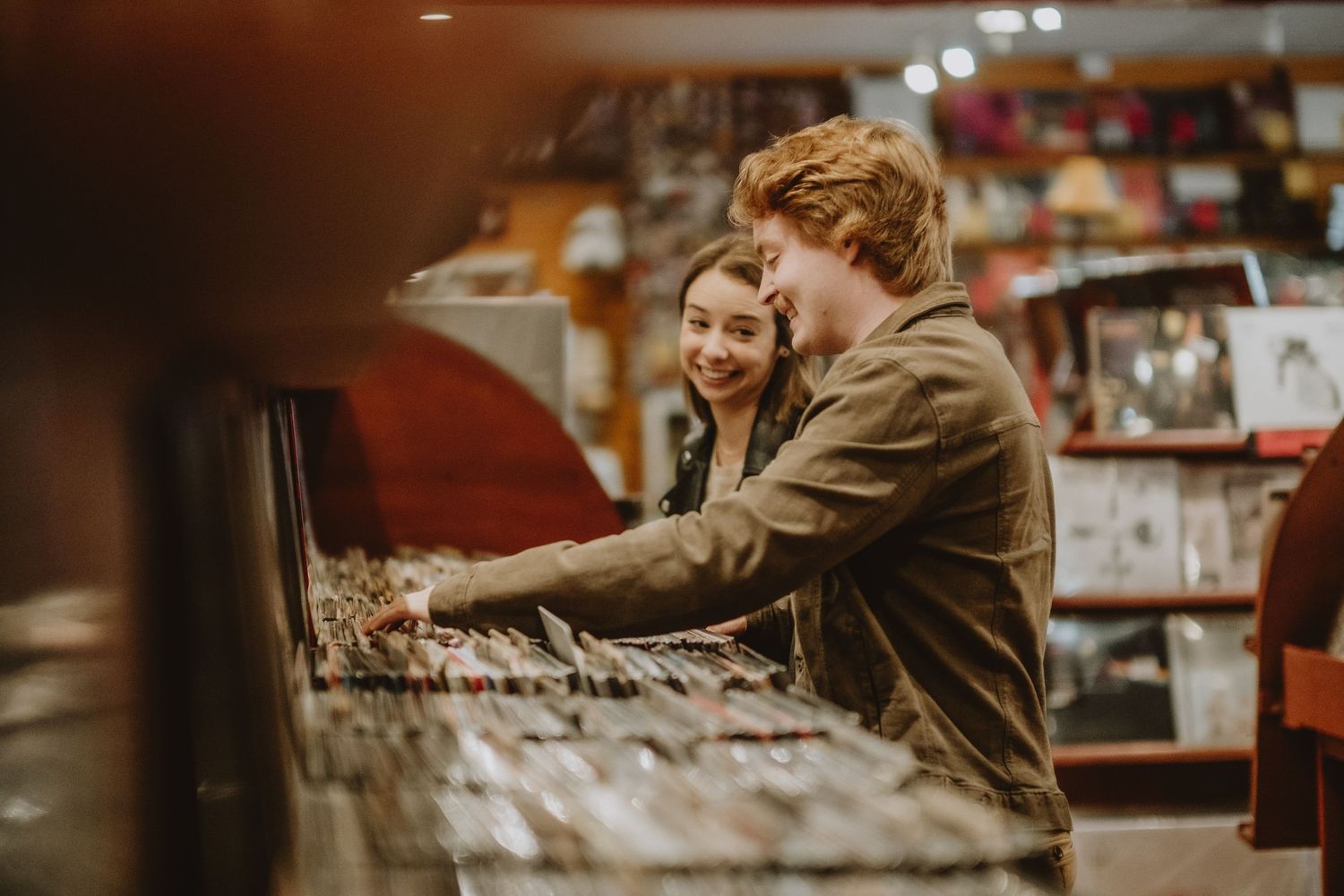 Two people browse through vinyl records together at a music store in warm lighting.