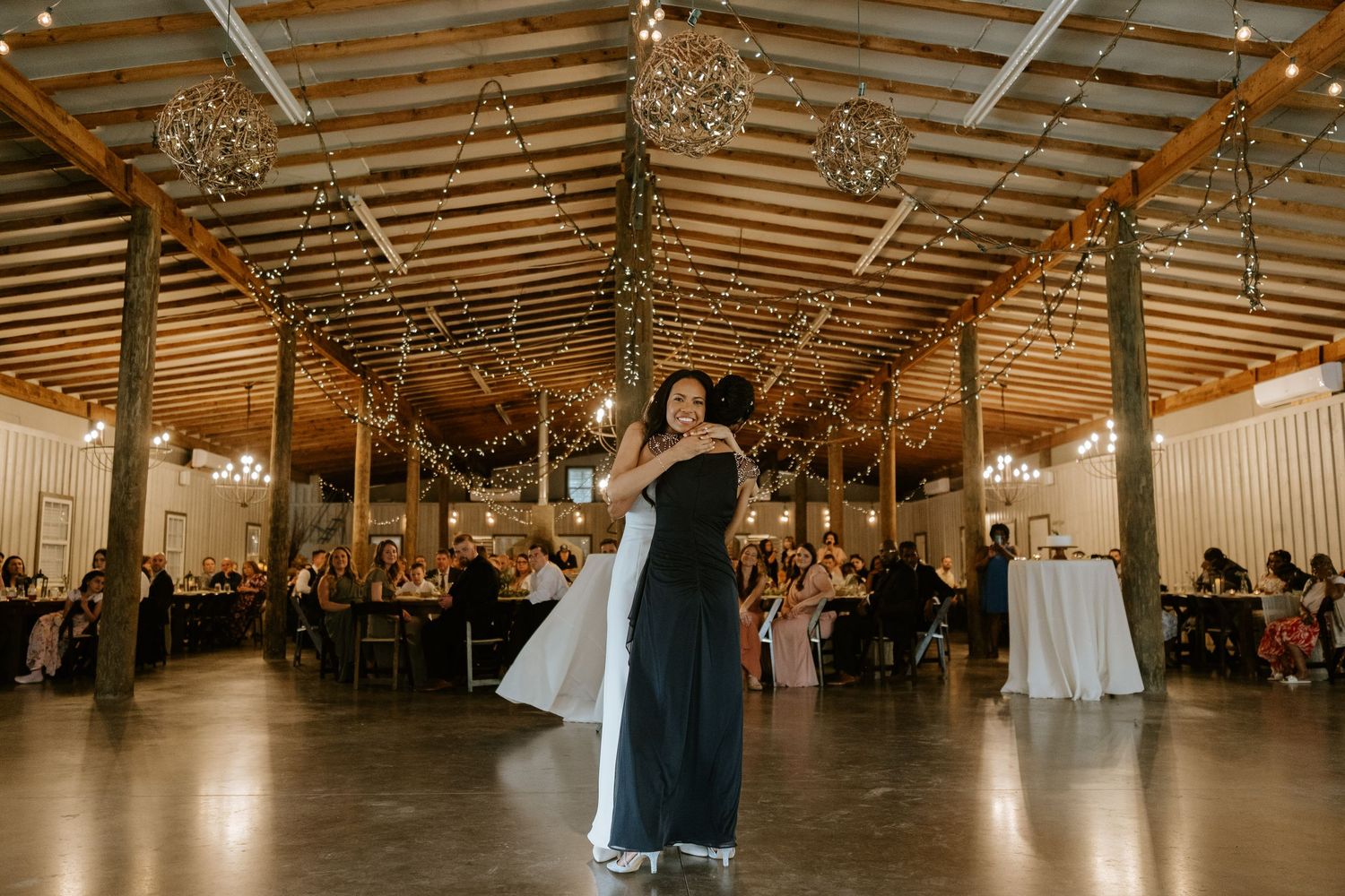 Panoramic view of an elegant rustic barn wedding reception with exposed wooden beams and hanging crystal chandeliers.