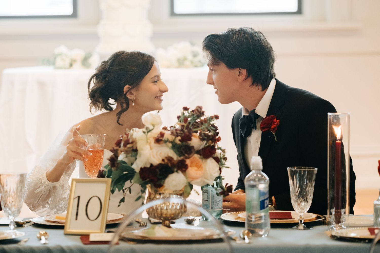 Elegant wedding reception table setting with guests seated in a bright white venue.