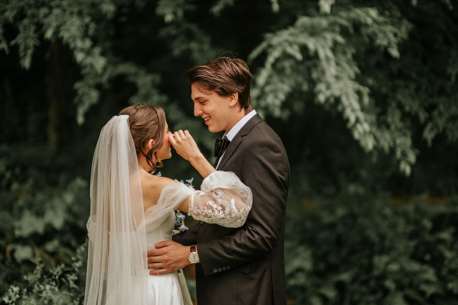 An intimate wedding portrait showing tender embrace against a backdrop of evergreen trees.