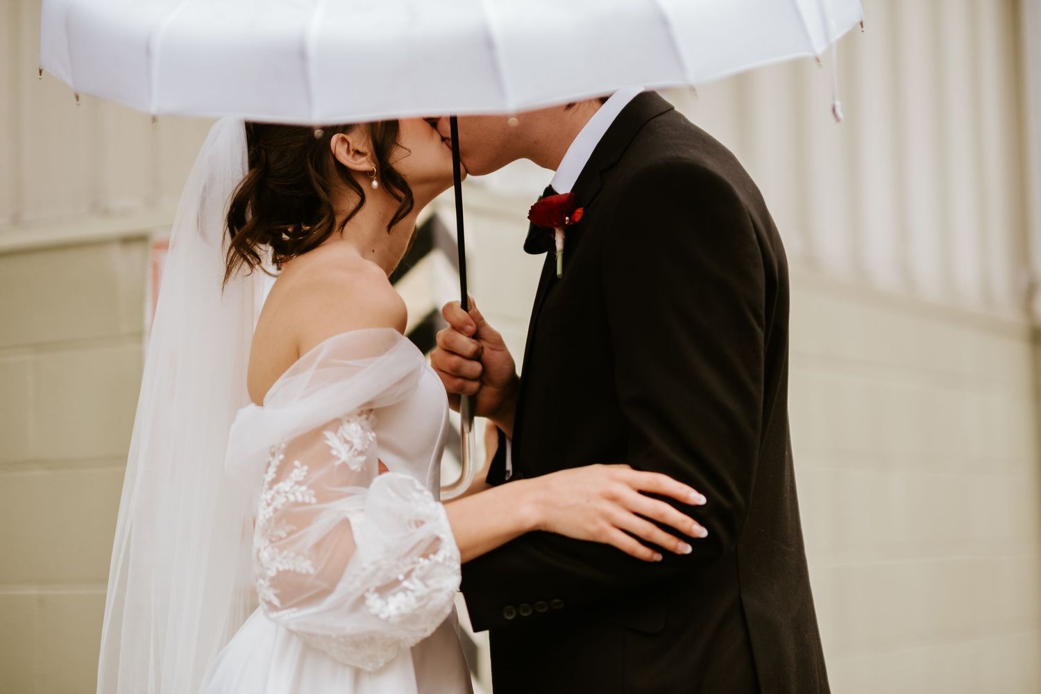 A romantic wedding couple shares an intimate moment in a rustic setting with white decor.