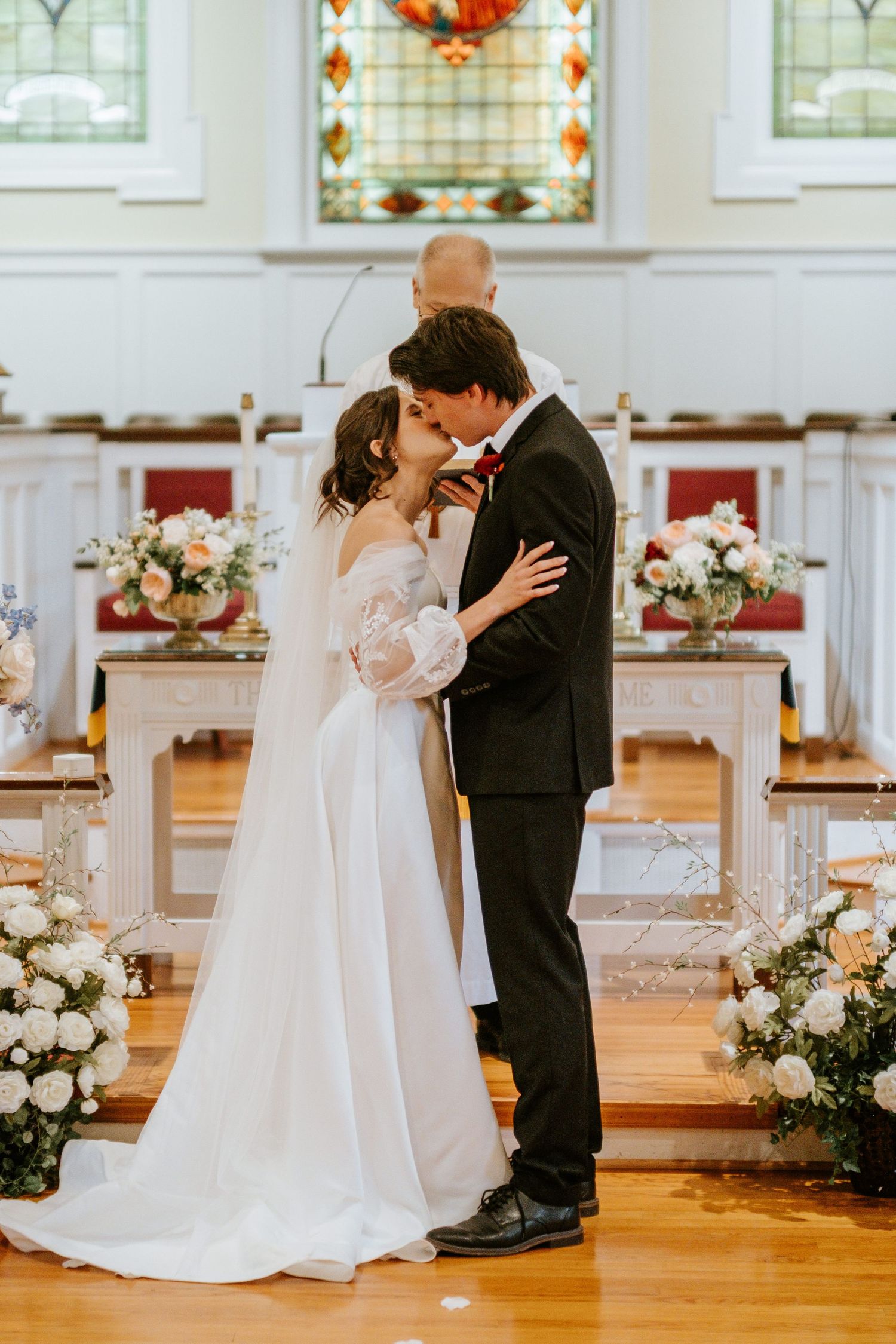 A romantic wedding moment captured in a bright church with stained glass windows and floral decorations.