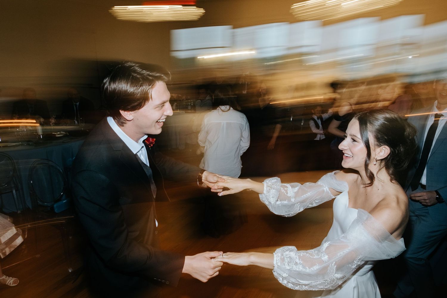 Motion-blurred dance floor scene at wedding reception with warm ambient lighting.