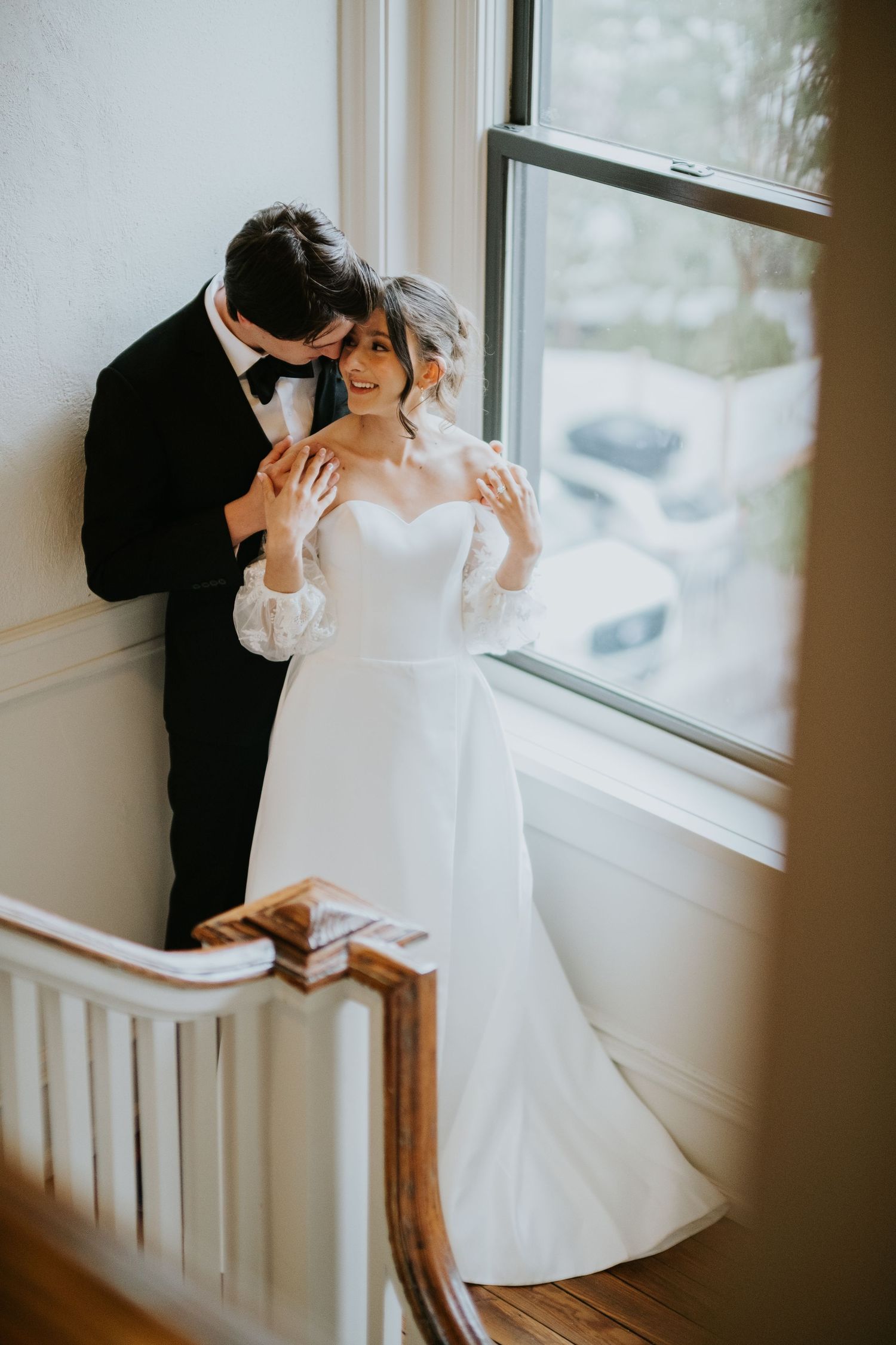 A romantic moment captured by a window with natural light illuminating a couple in wedding attire.