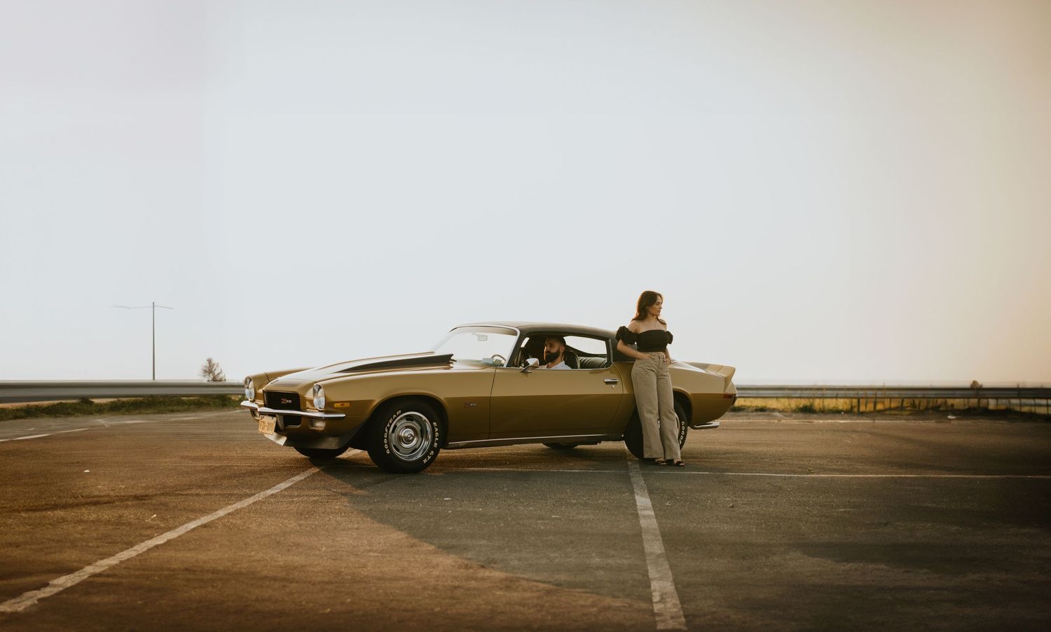A vintage brown car parked in a desert landscape during sunset creates a nostalgic retro scene.