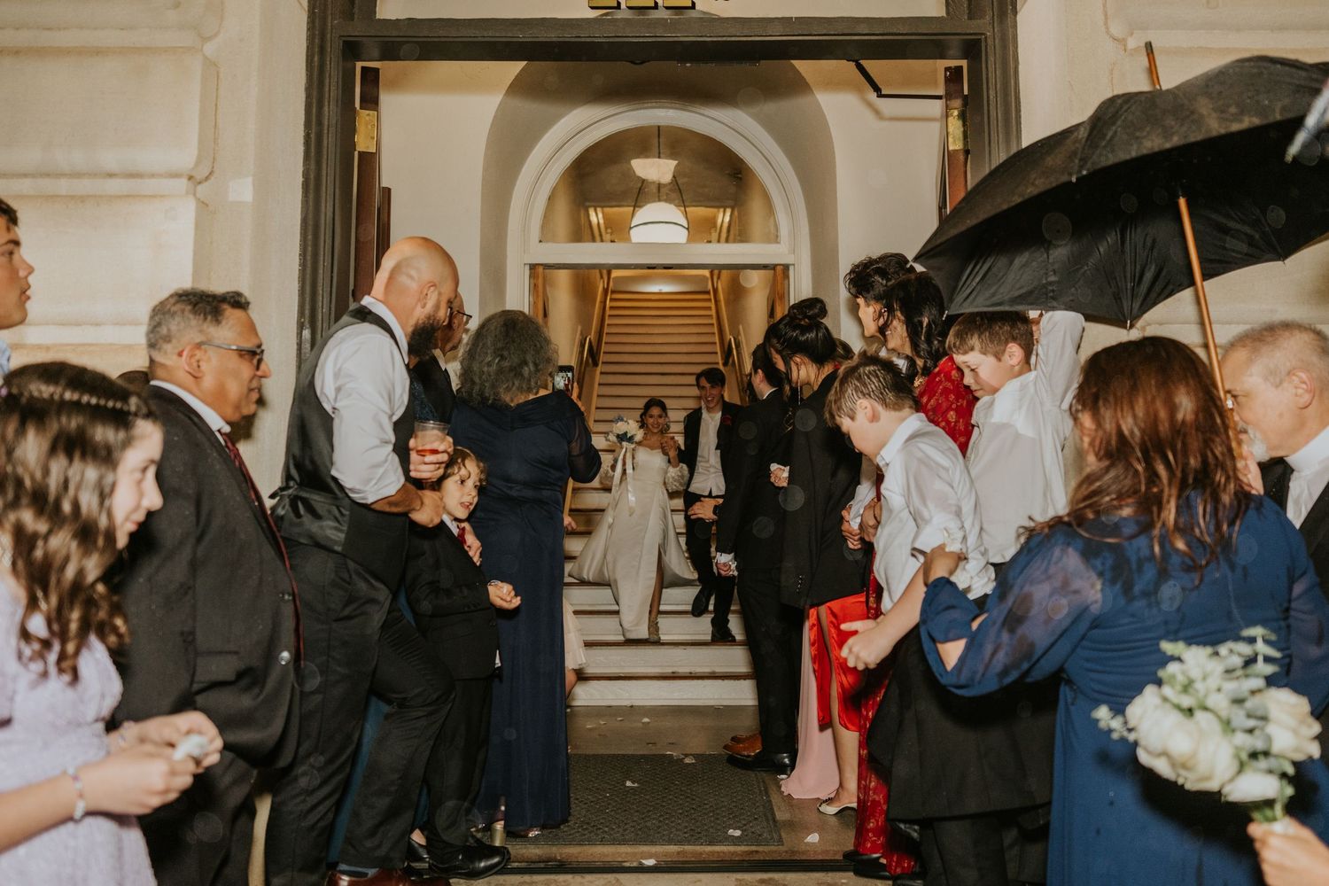 Wedding guests gather outside a church entrance as a couple exits after their ceremony on a rainy day.