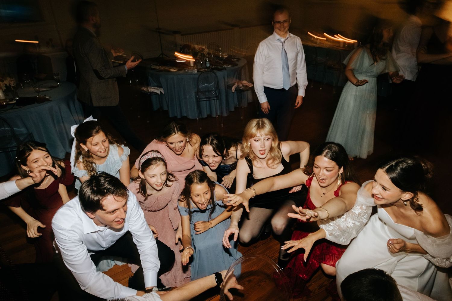 Wedding guests dance enthusiastically on the dance floor during a lively reception celebration.