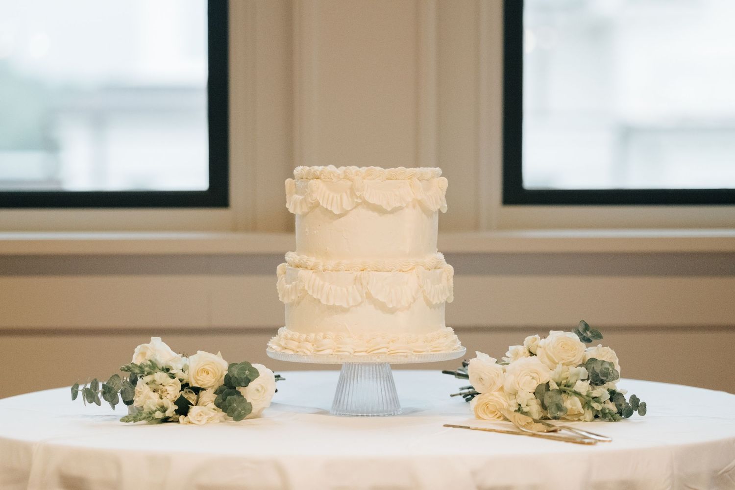 Three elegant white wedding cakes with ornate decorations displayed in a row on a light-colored surface.