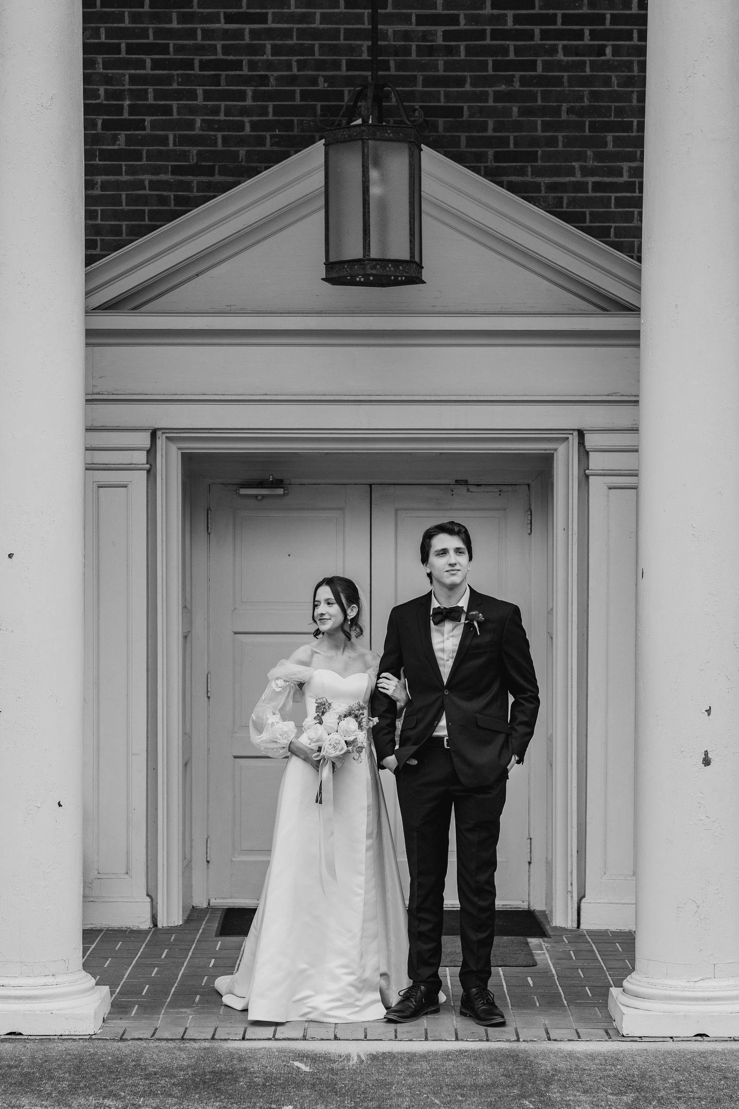 A classic black and white wedding portrait of a couple standing in front of an elegant doorway with a lantern above.