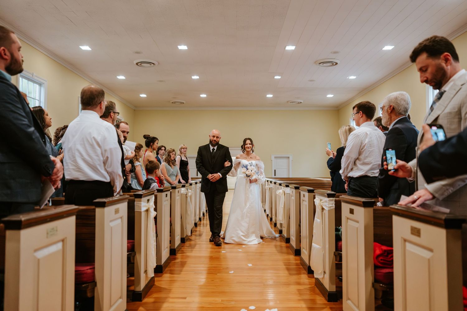 Wedding ceremony in progress down church aisle with wooden pews.
