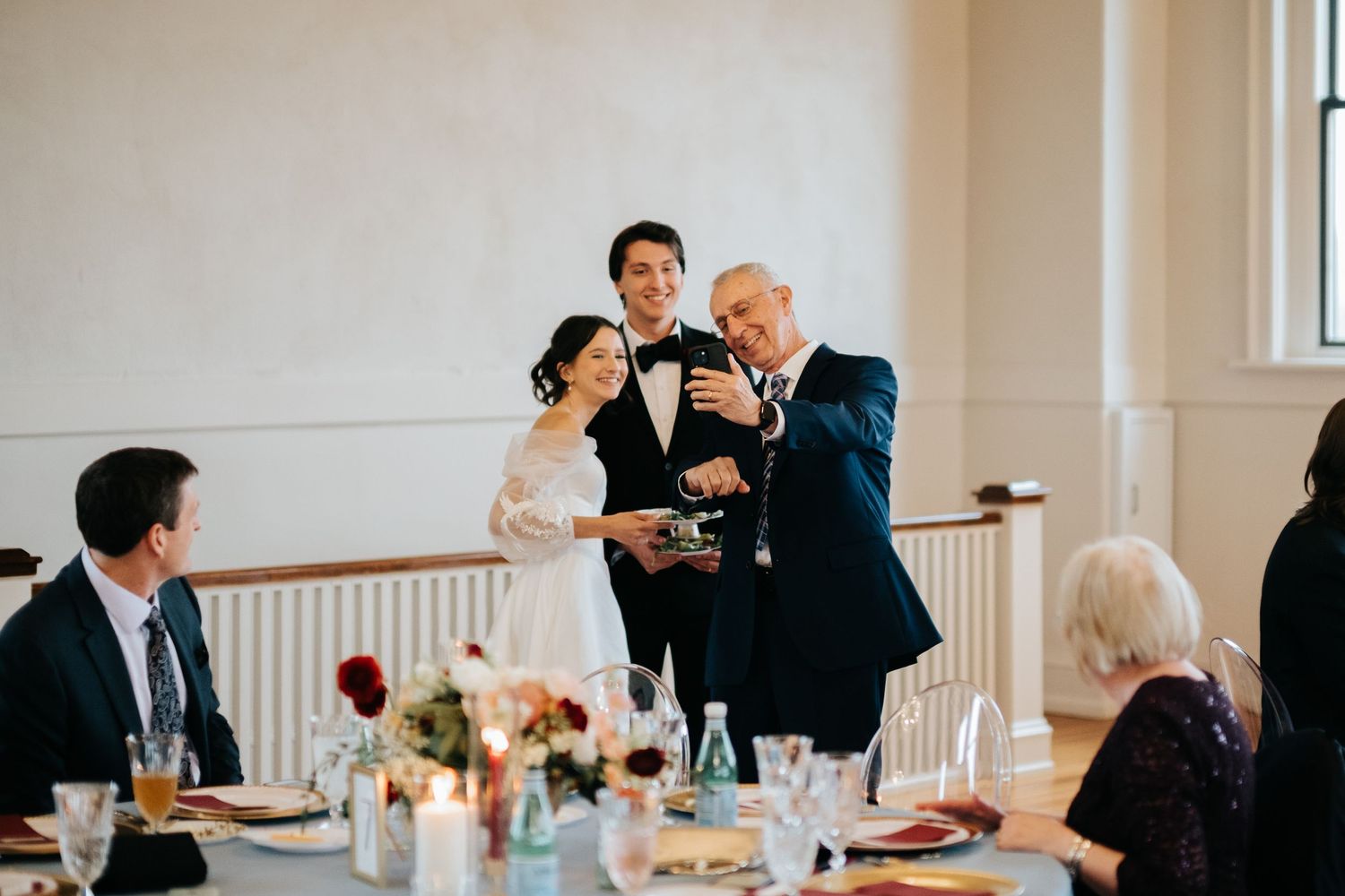Guests gather at a formal event in an elegant room with hardwood floors and white walls.