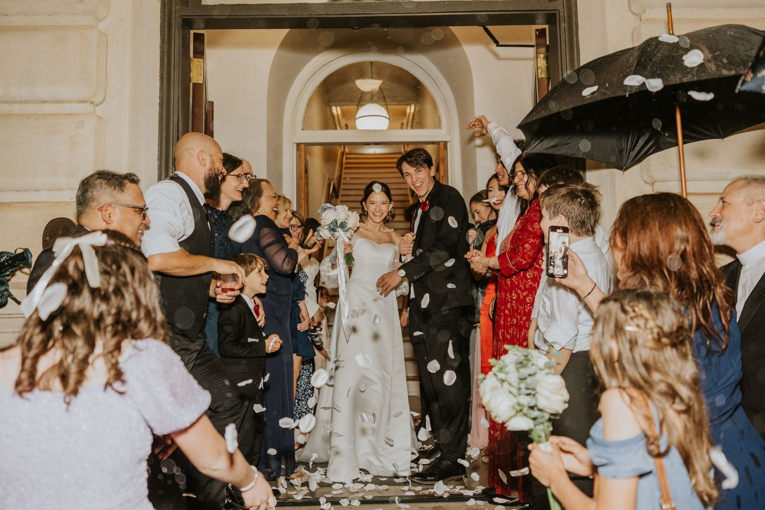 Newlyweds exit church as guests throw confetti in joyous wedding celebration.