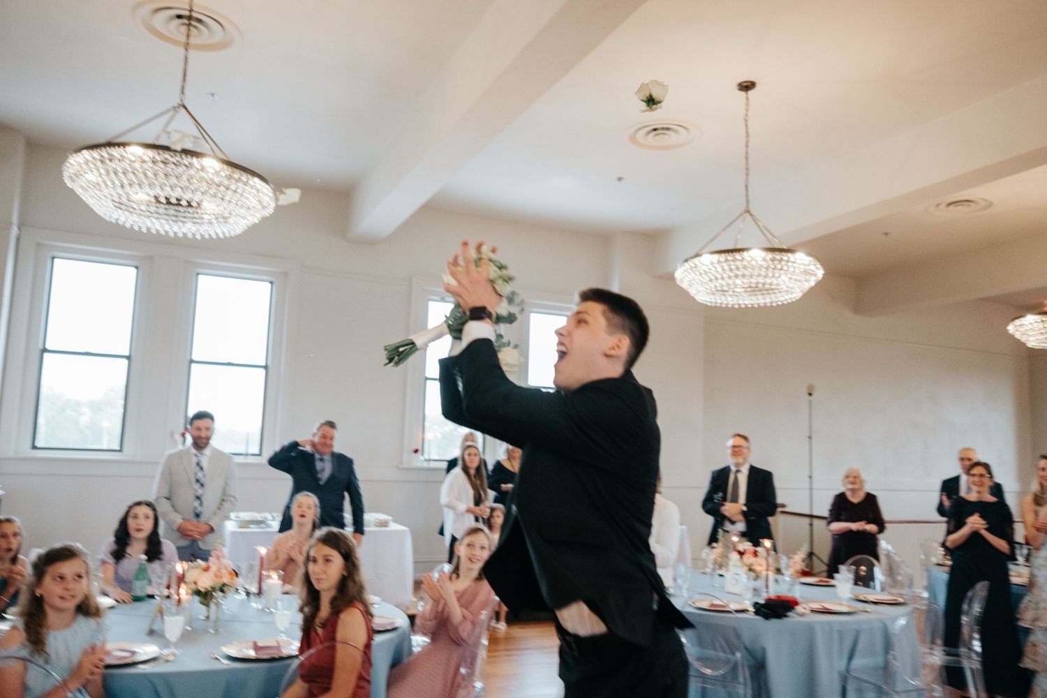 Wedding guest enthusiastically dancing and celebrating at an elegant reception with crystal chandeliers.