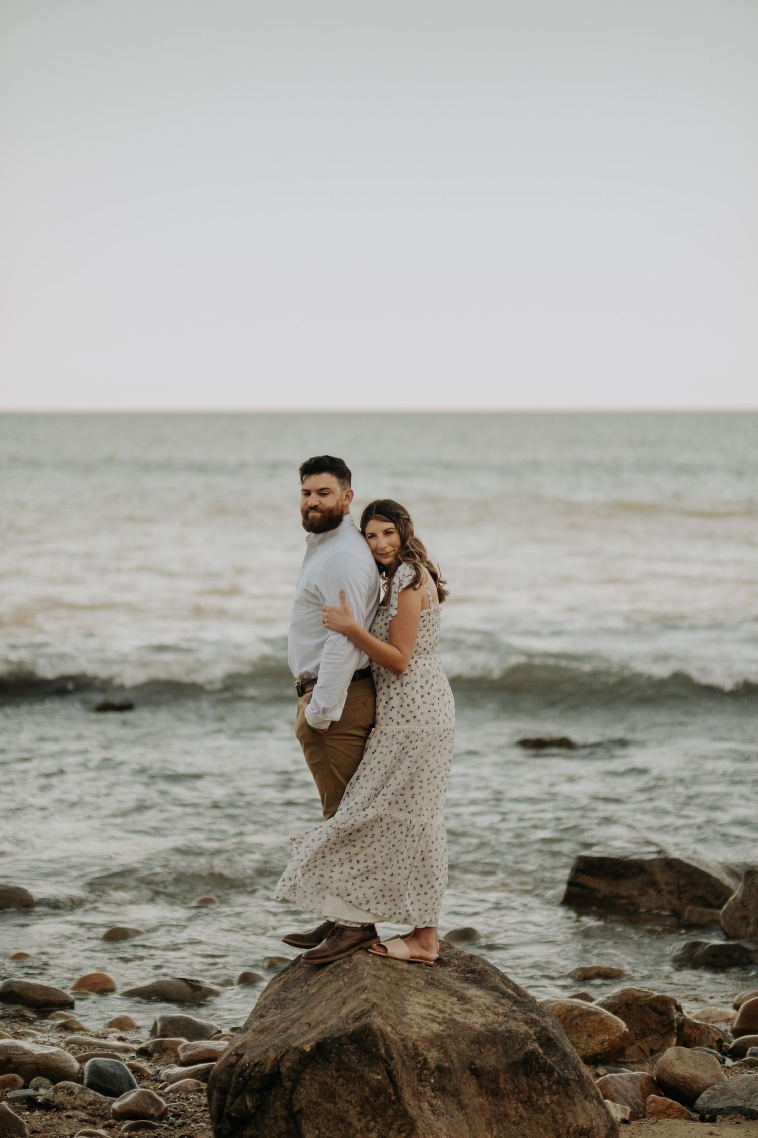 A couple embraces on rocky coastal shoreline at dusk in romantic seaside photoshoot.