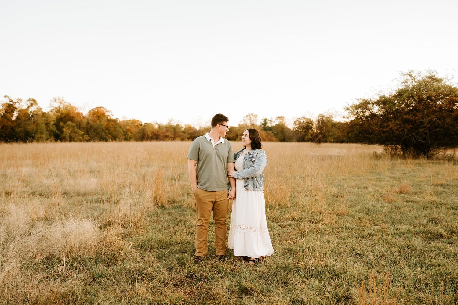 A couple walks hand in hand through a golden field at sunset during a romantic photoshoot.