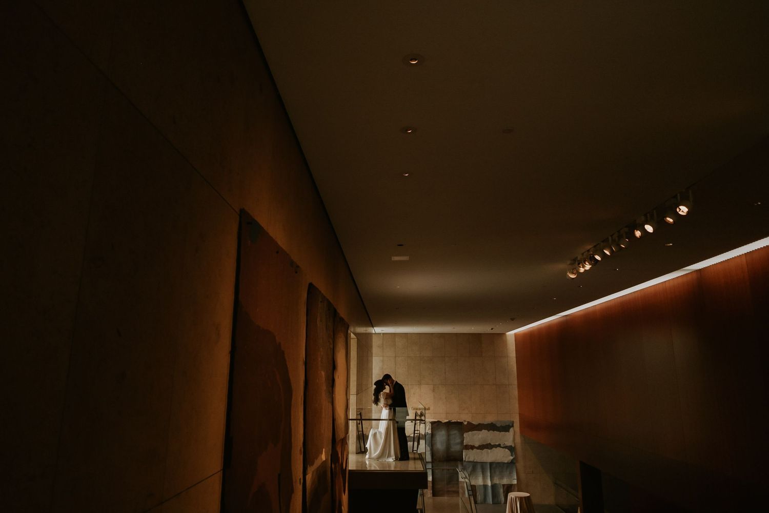 Couple sharing a romantic moment on a dimly lit balcony inside an elegant venue with warm lighting.