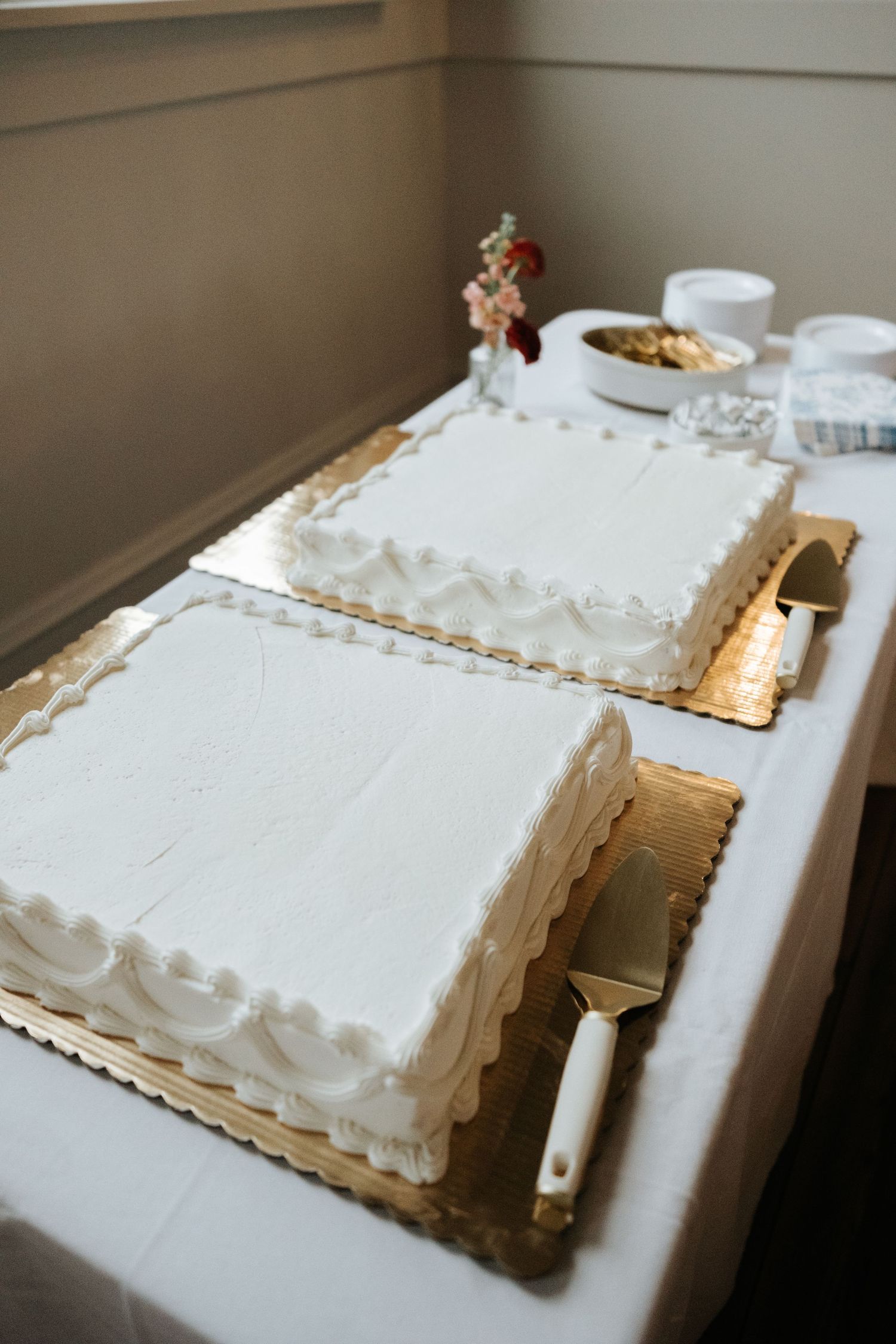White frosted sheet cakes with gold trim arranged in a row on display table.