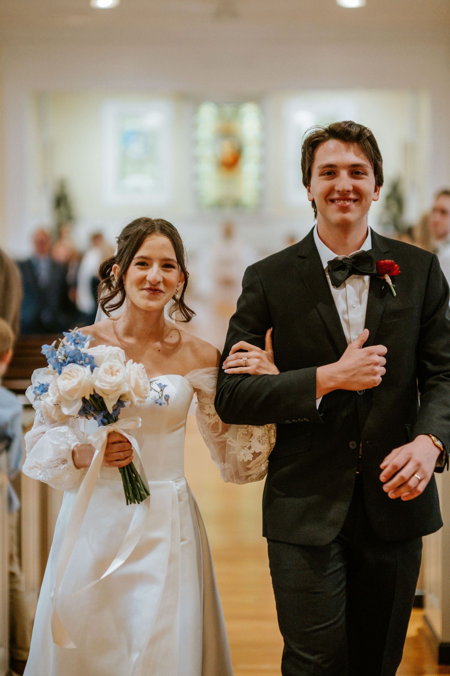 Wedding couple walks arm in arm down a bright hallway during their reception celebration.