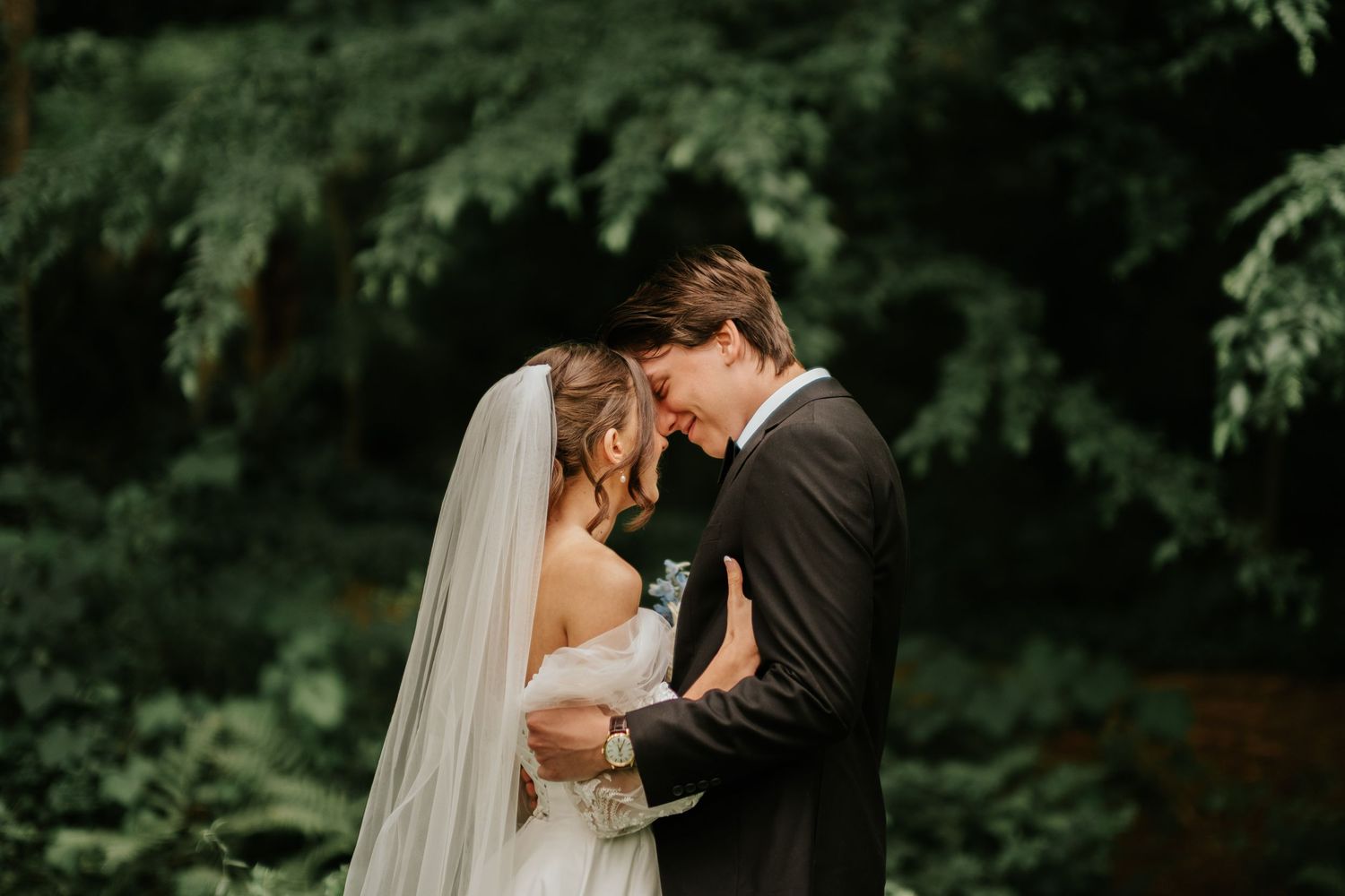 Newlywed couple shares intimate moment in lush green garden setting during outdoor wedding ceremony.