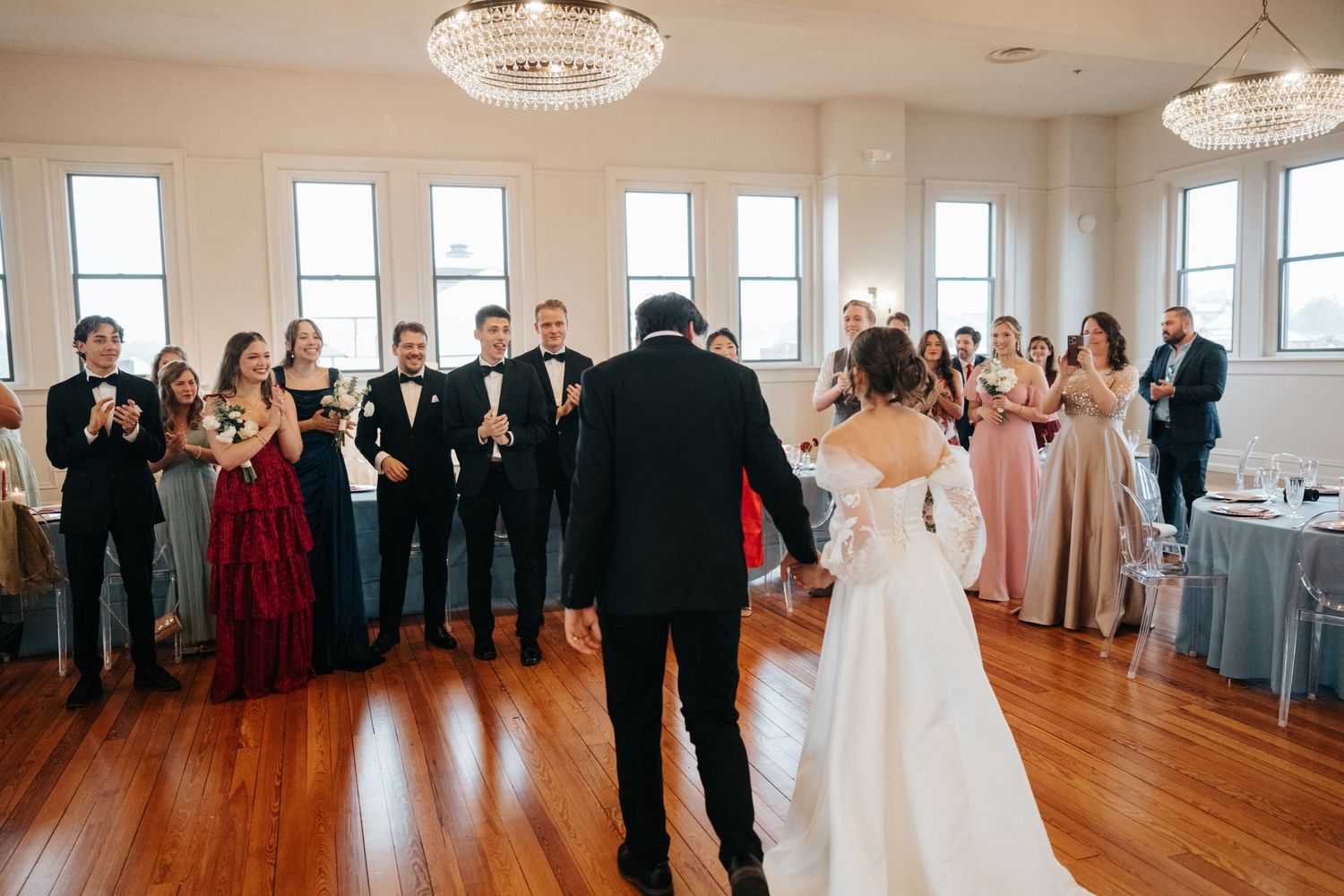 Wedding couple receiving applause from guests during their first dance in an elegant reception hall.